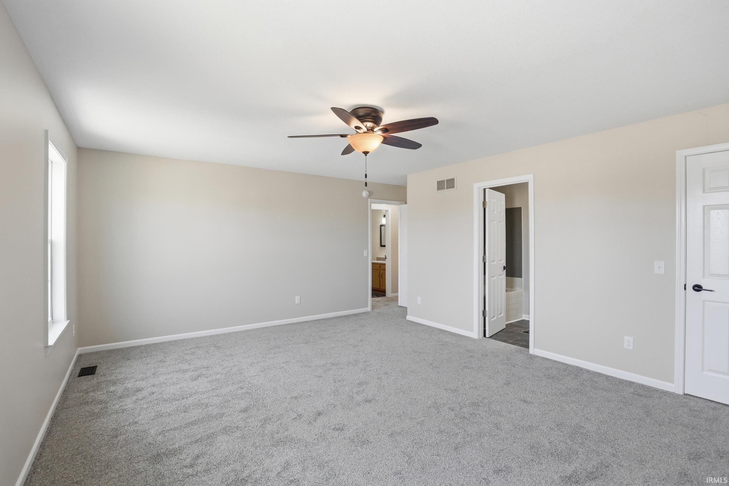 Unfurnished bedroom with ensuite bath, ceiling fan, and light carpet