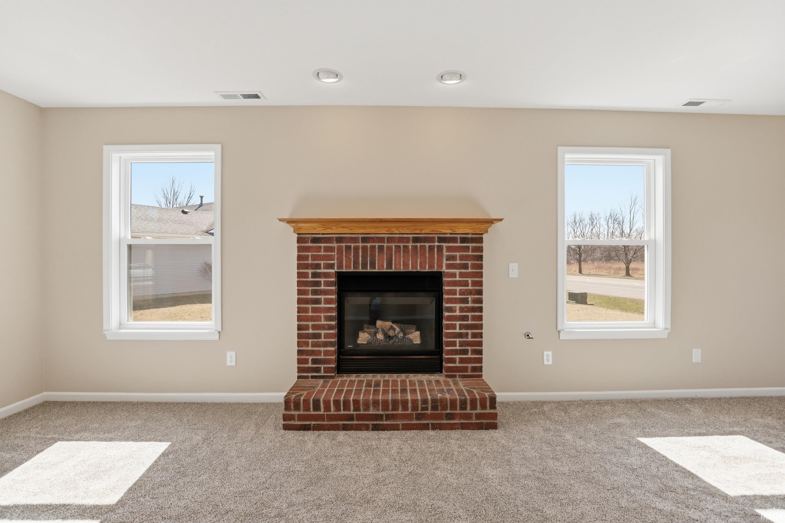 Unfurnished living room featuring light carpet, a fireplace, and healthy amount of natural light