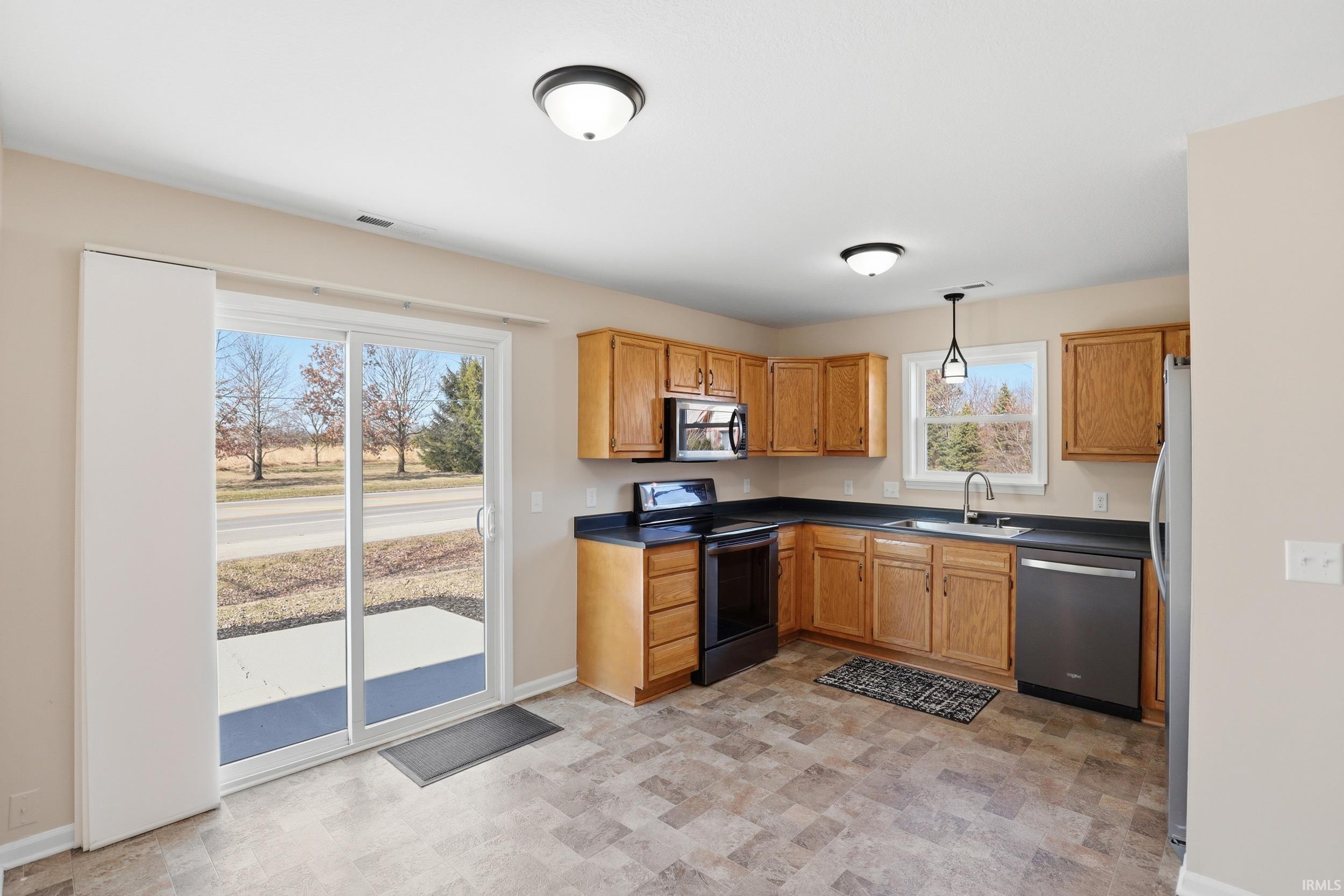 Kitchen with dark countertops, stainless steel appliances, wood finish cabinetry, decorative light fixtures, and stone finish flooring