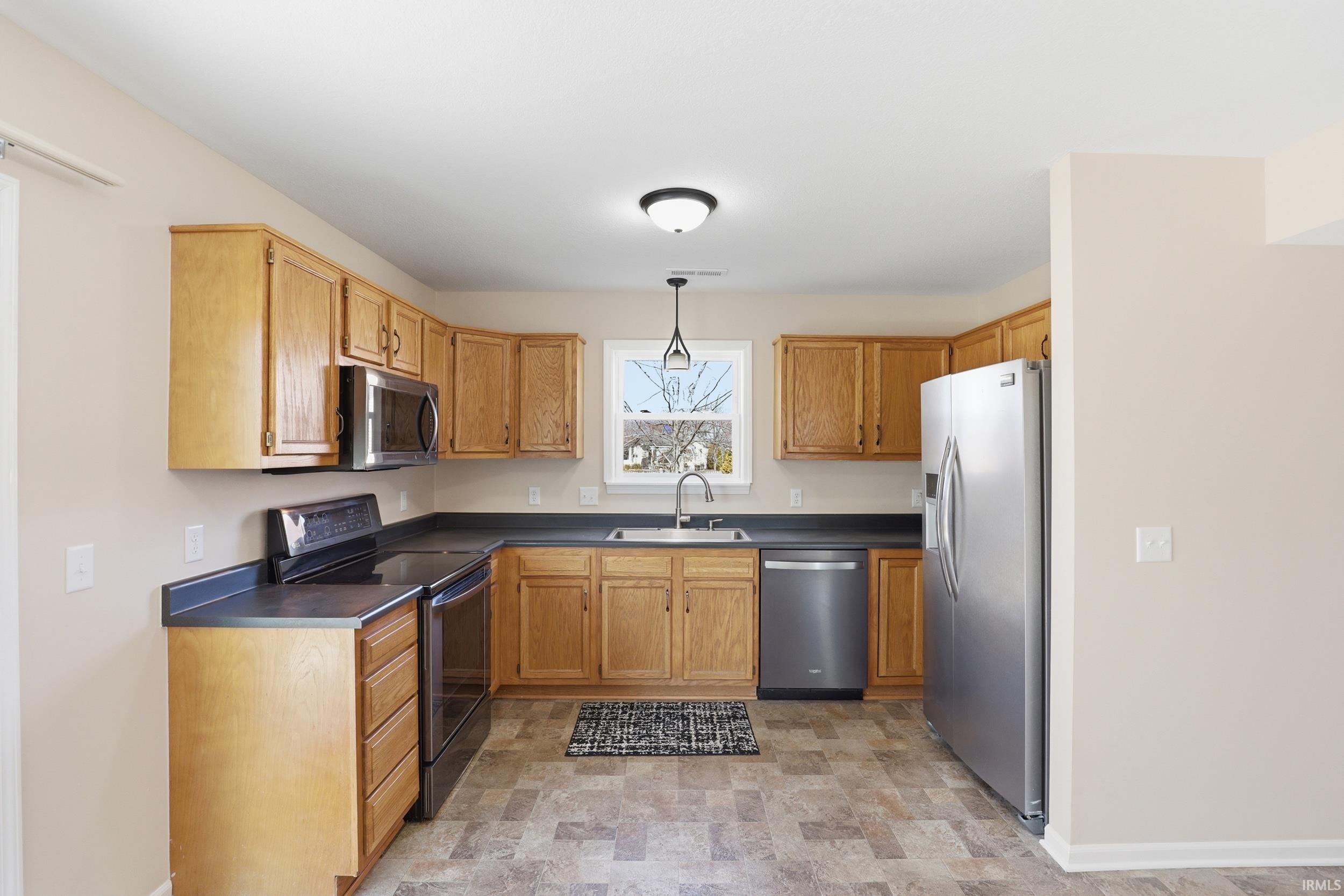 Kitchen featuring dark countertops, stone finish flooring, stainless steel appliances, hanging light fixtures, and wood finish cabinetry