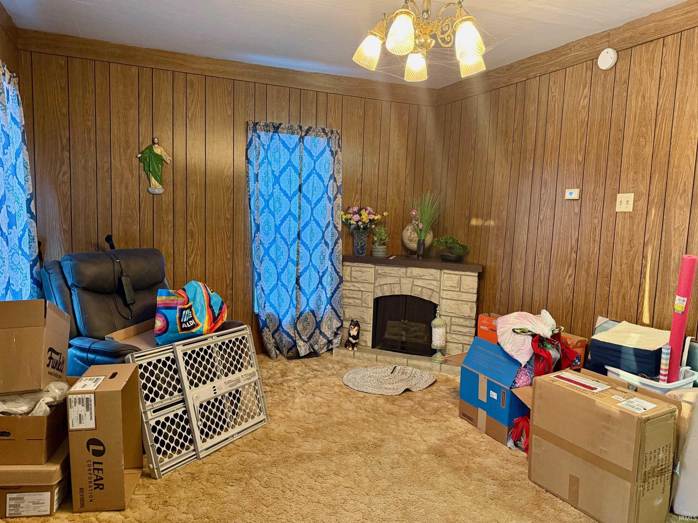 Living area featuring carpet floors, a stone fireplace, hanging lights, and wooden walls