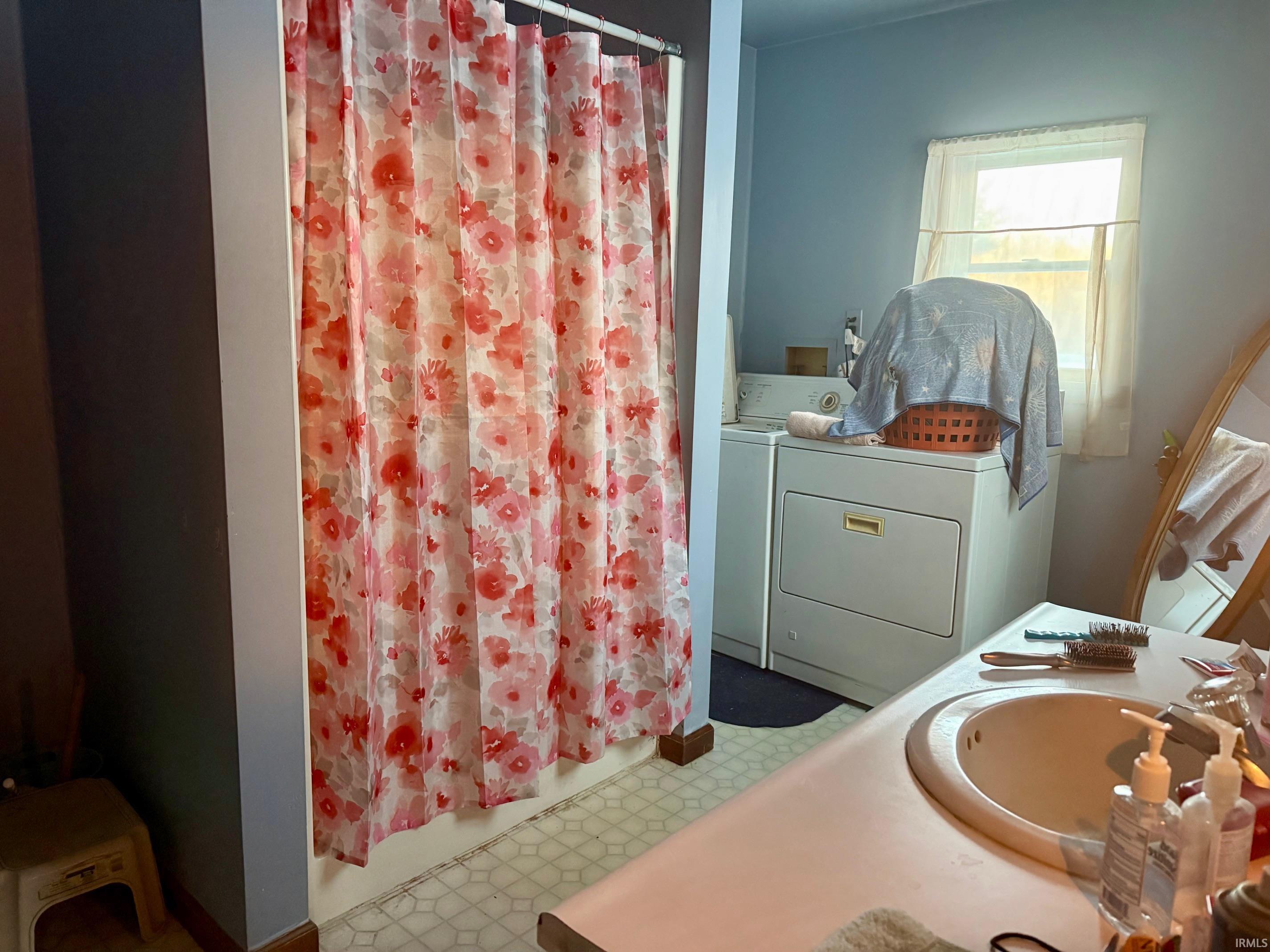 Bathroom featuring a shower with shower curtain, washing machine and clothes dryer, vanity, and tile patterned floors