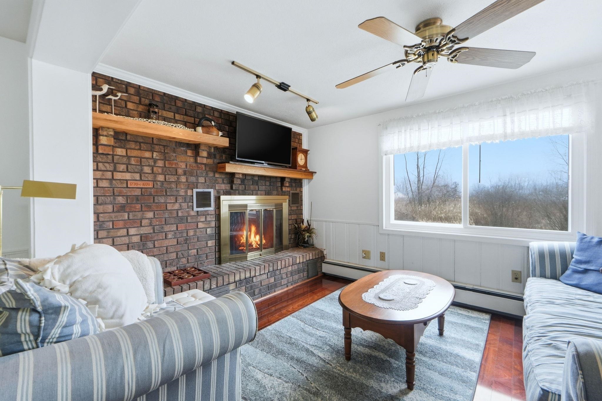 Living room featuring track lighting, wood finished floors, a baseboard heating unit, ceiling fan, and a fireplace