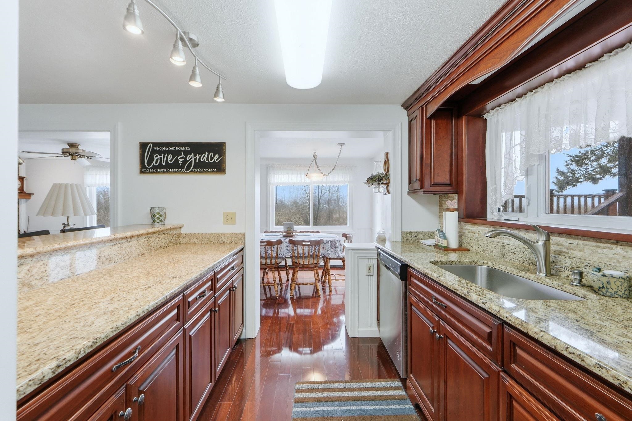 Kitchen featuring light stone counters, bold wood finish cabinets, dark wood finished floors, and dishwasher