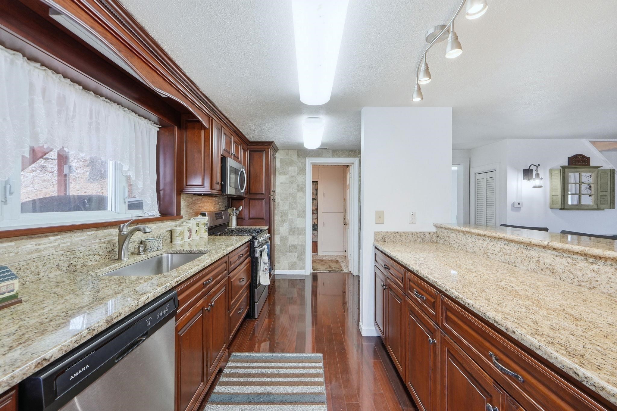 Kitchen with stainless steel appliances, light stone counters, dark wood finished floors, and a textured ceiling