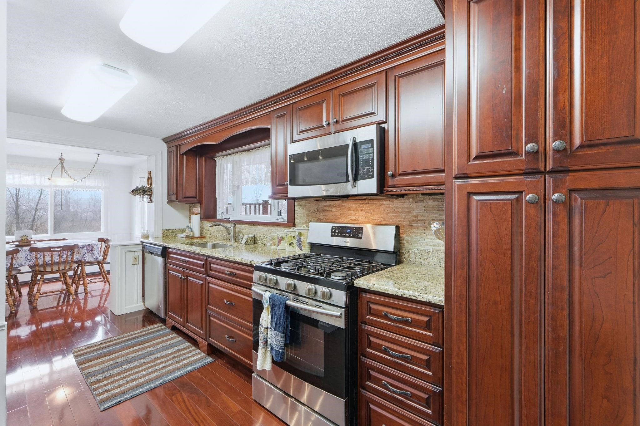 Kitchen featuring stainless steel appliances, light stone counters, tasteful backsplash, and dark wood-type flooring