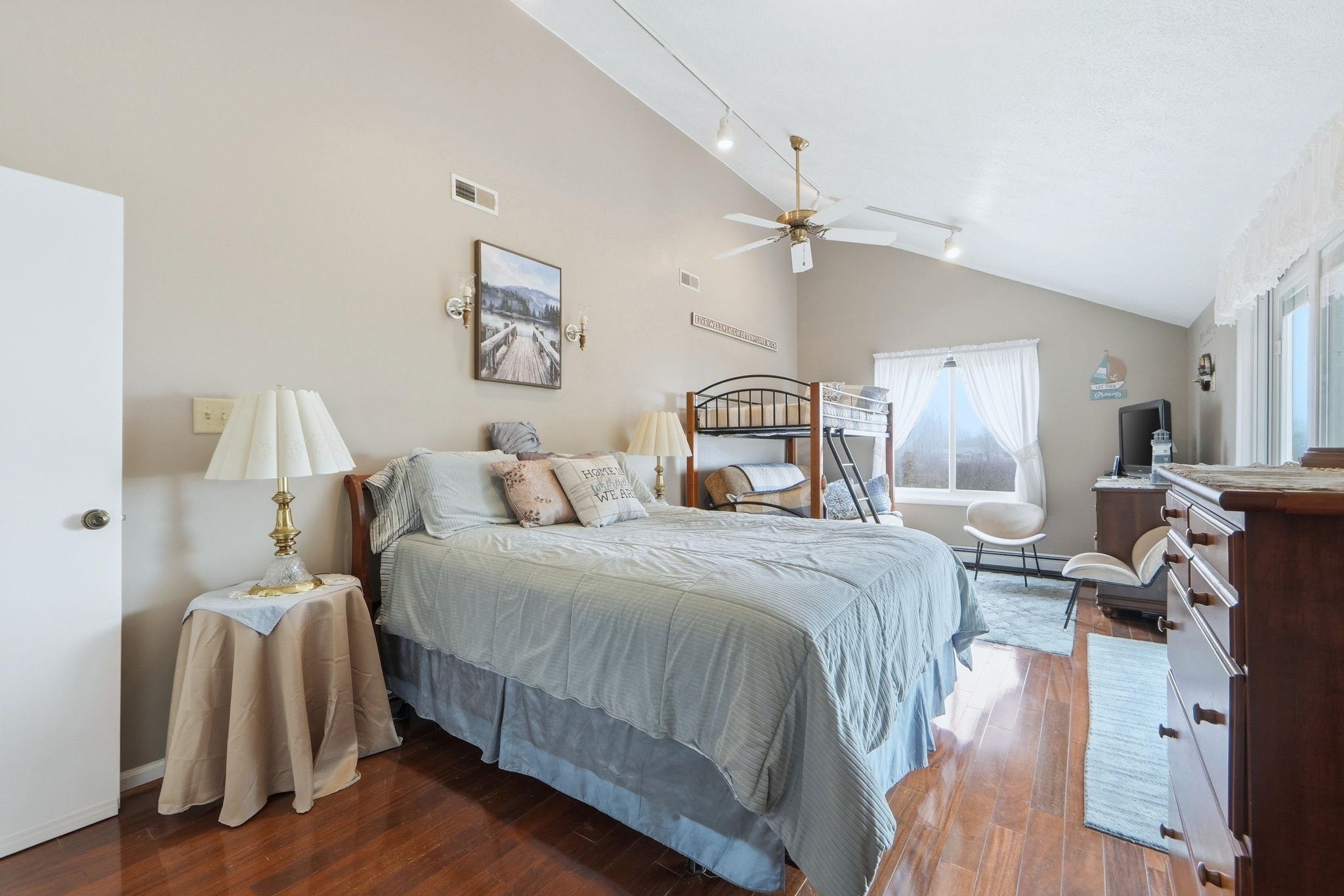 Bedroom with track lighting, vaulted ceiling, wood finished floors, ceiling fan, and baseboard heating