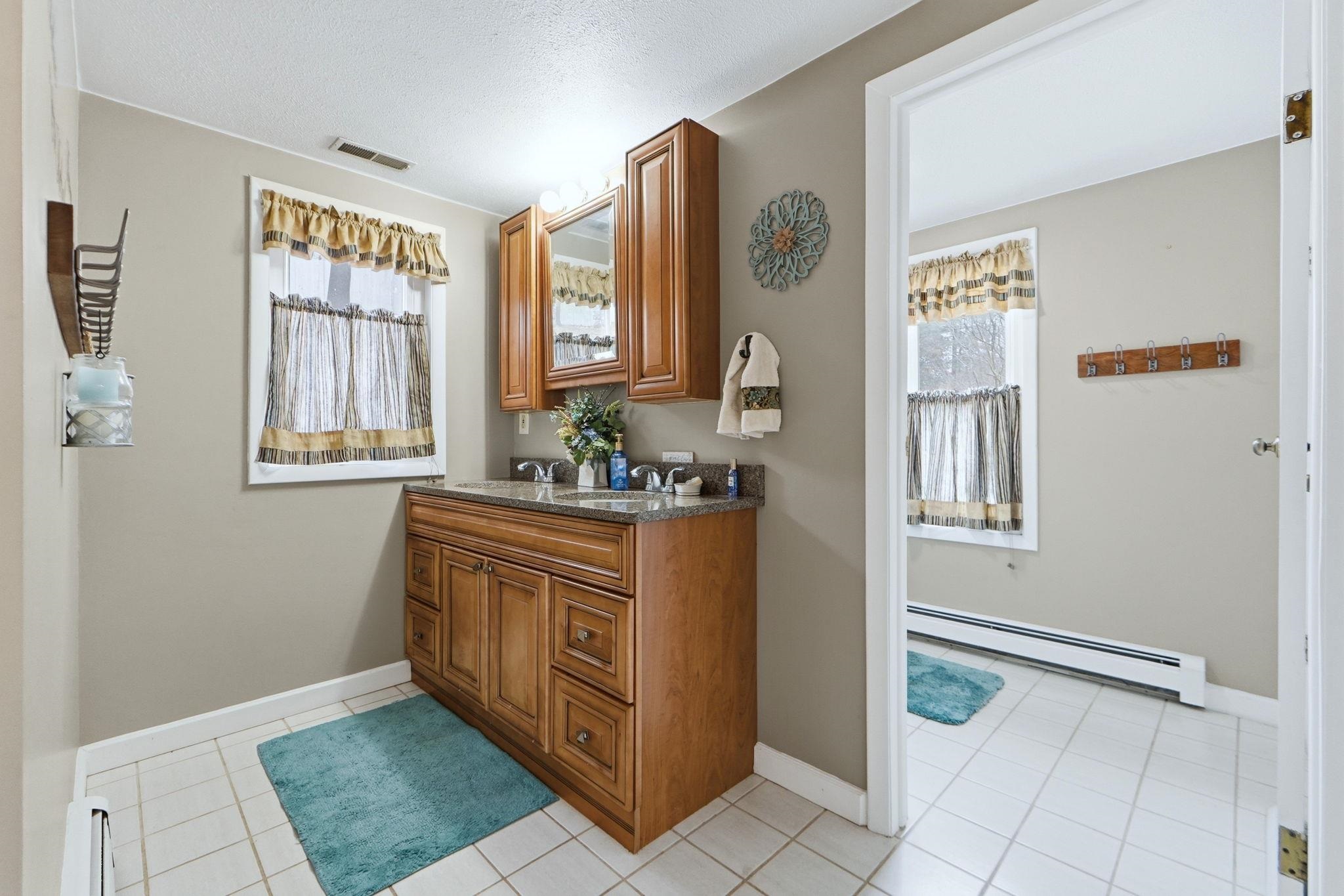 Full bath with double vanity, baseboard heating, light tile patterned flooring, healthy amount of natural light, and a textured ceiling