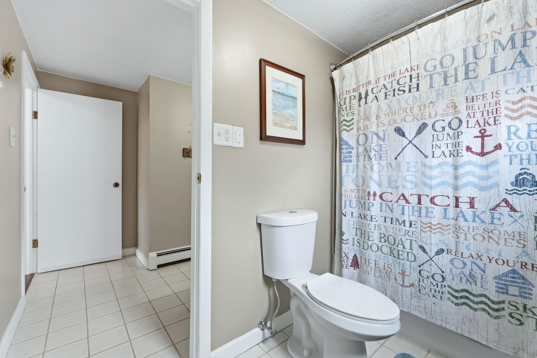 Full bathroom featuring light tile patterned floors, a shower with shower curtain, baseboard heating, and a textured ceiling