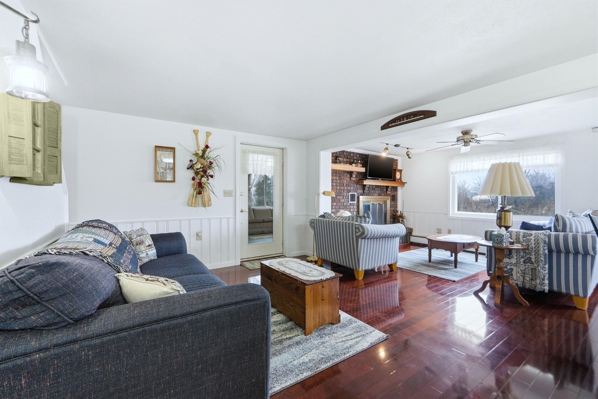 Living area featuring wainscoting, hardwood / wood-style flooring, a ceiling fan, a brick fireplace, and baseboard heating