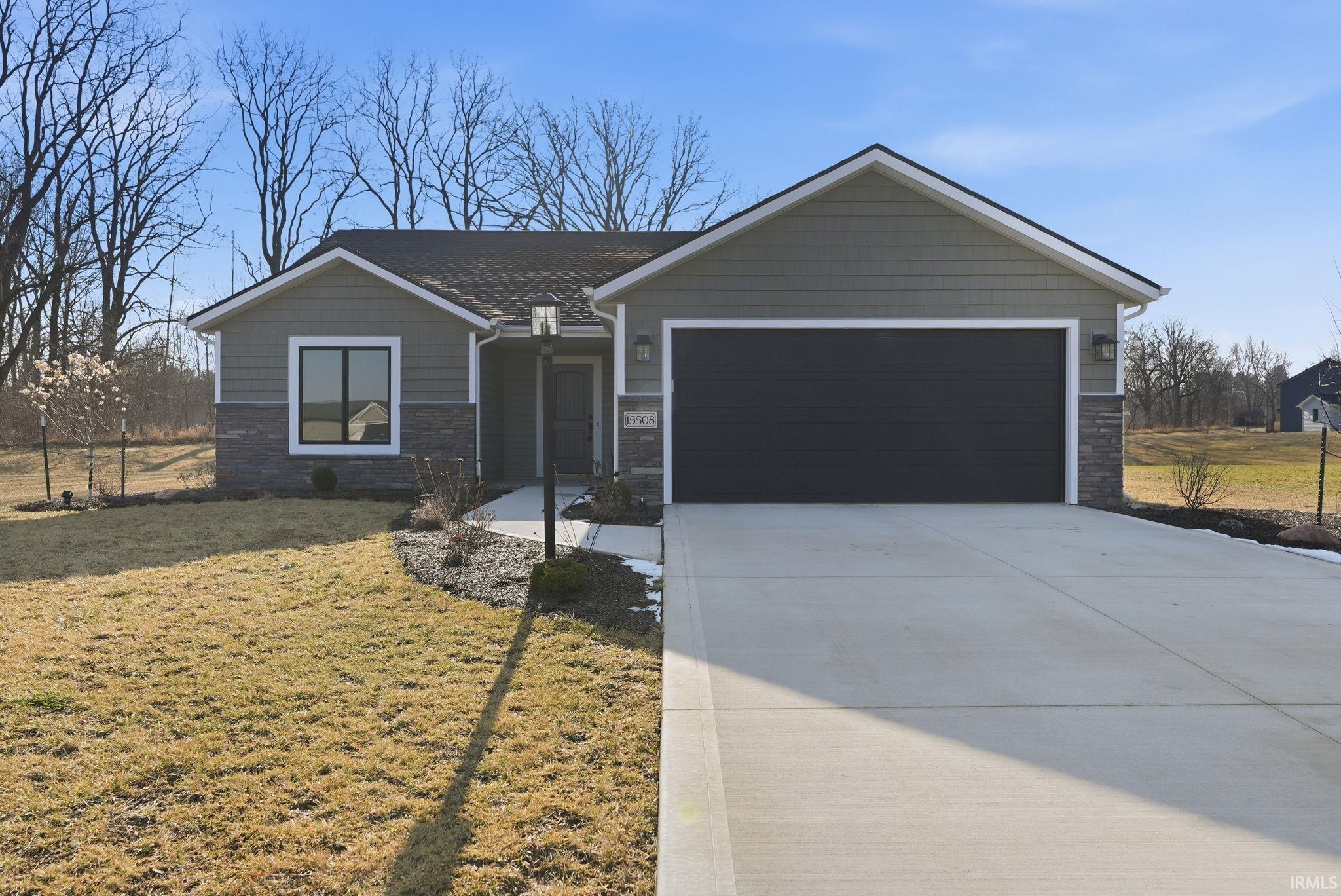 Single story home featuring stone siding, a front lawn, an attached garage, and driveway