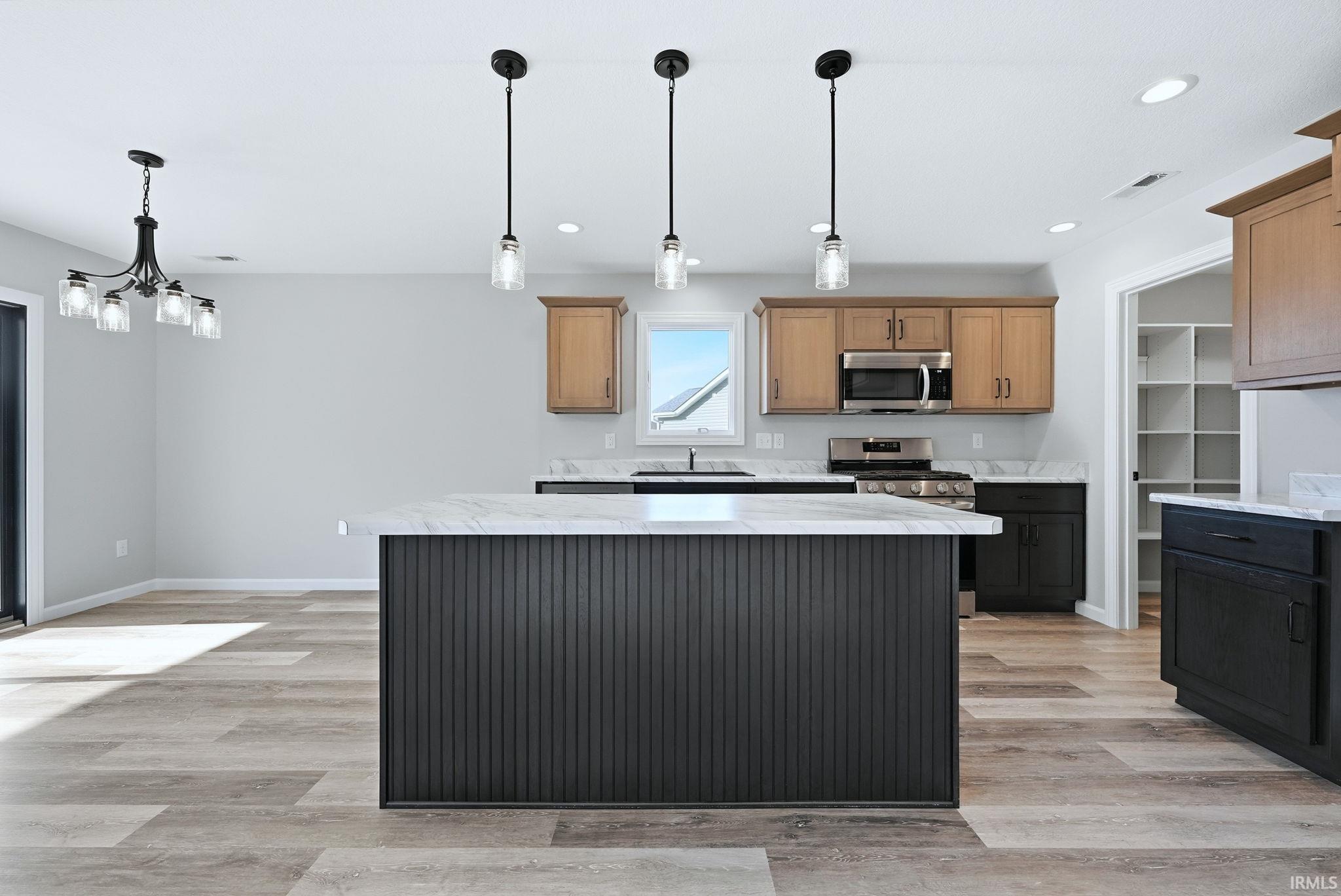 Kitchen with stainless steel appliances, light wood-style flooring, light stone countertops, a center island, and wood finish cabinetry