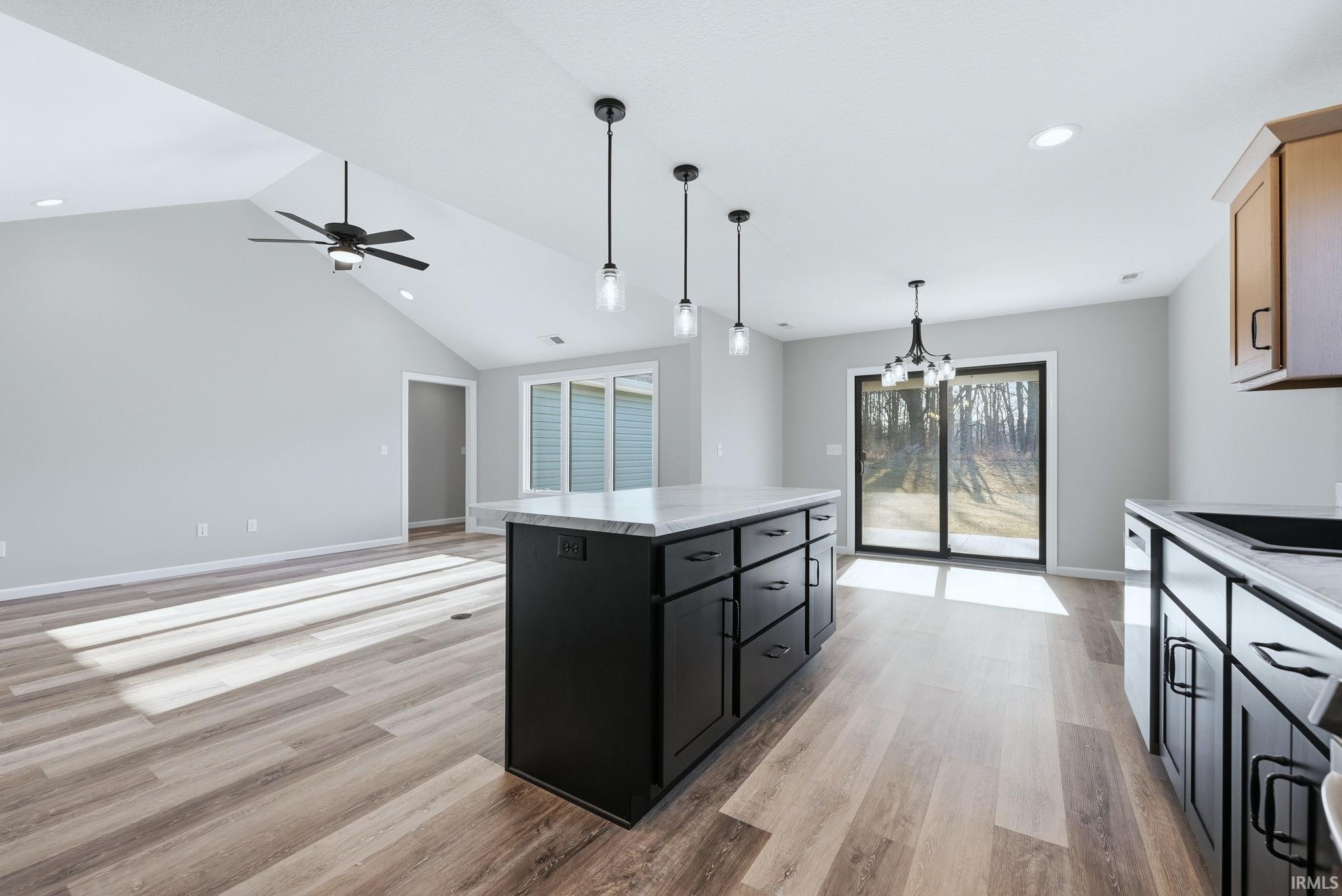 Kitchen featuring dark cabinets, hanging lights, a kitchen island, light wood-style floors, and open floor plan