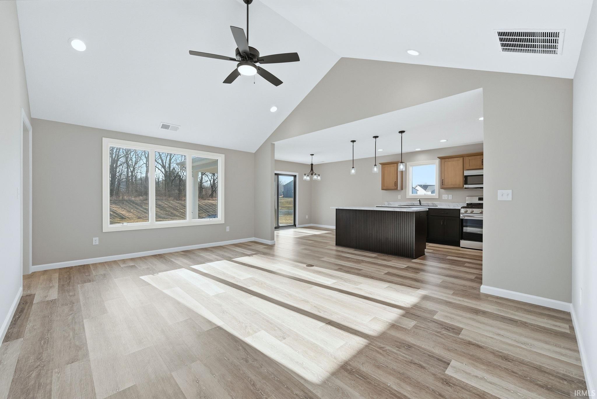 Living room with ceiling fan, a high ceiling, hanging lights, and light wood finished floors