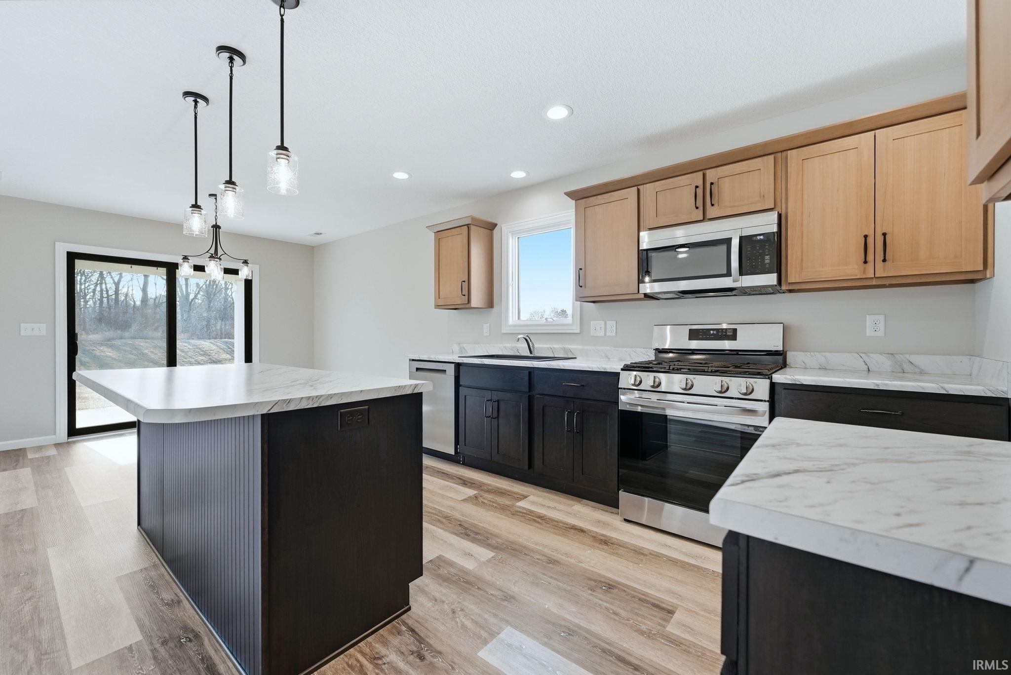 Kitchen featuring stainless steel appliances, light countertops, a kitchen island, pendant lighting, and light wood-style flooring