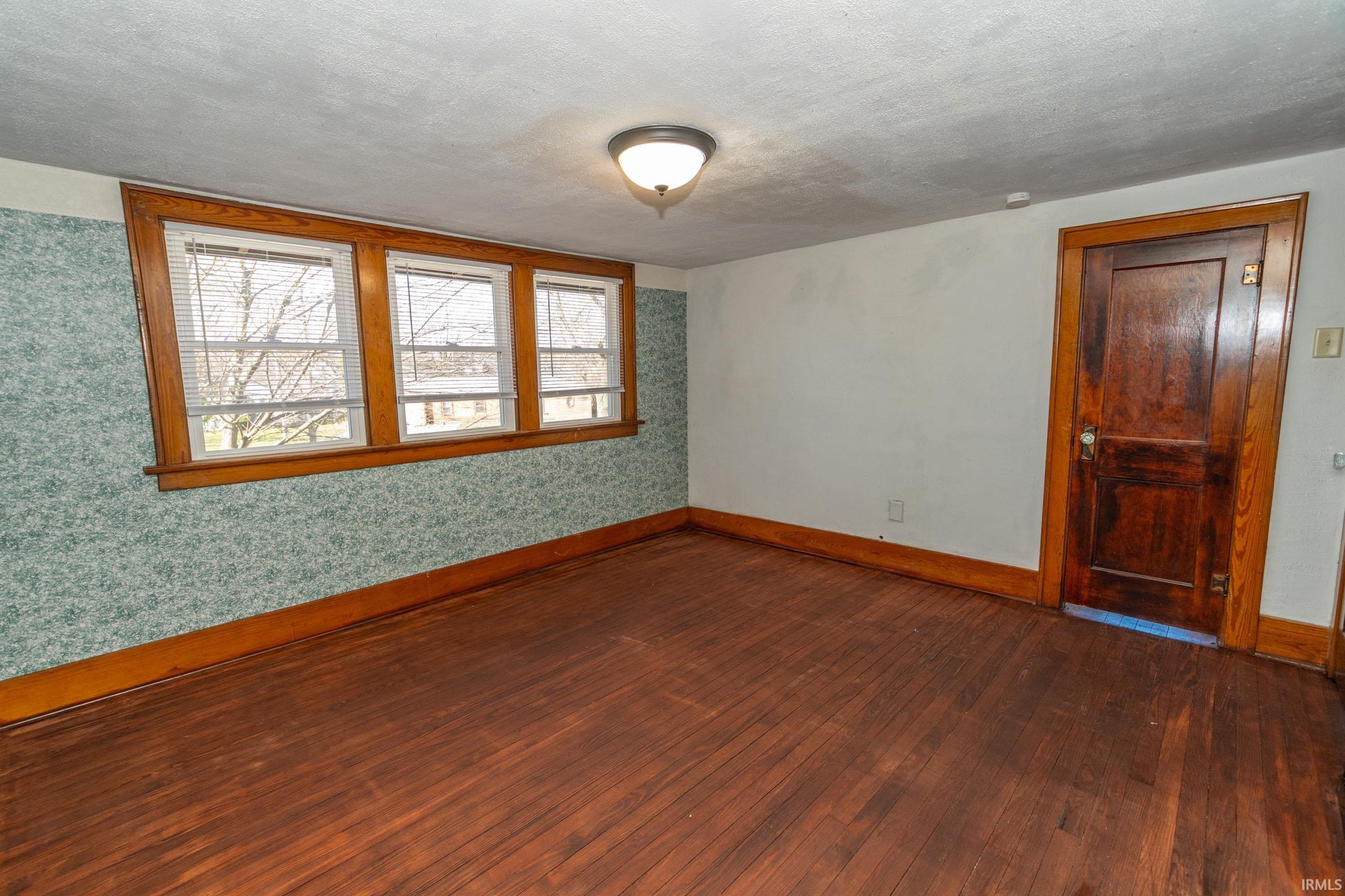Spare room with dark wood-style flooring, wallpapered walls, and a textured ceiling