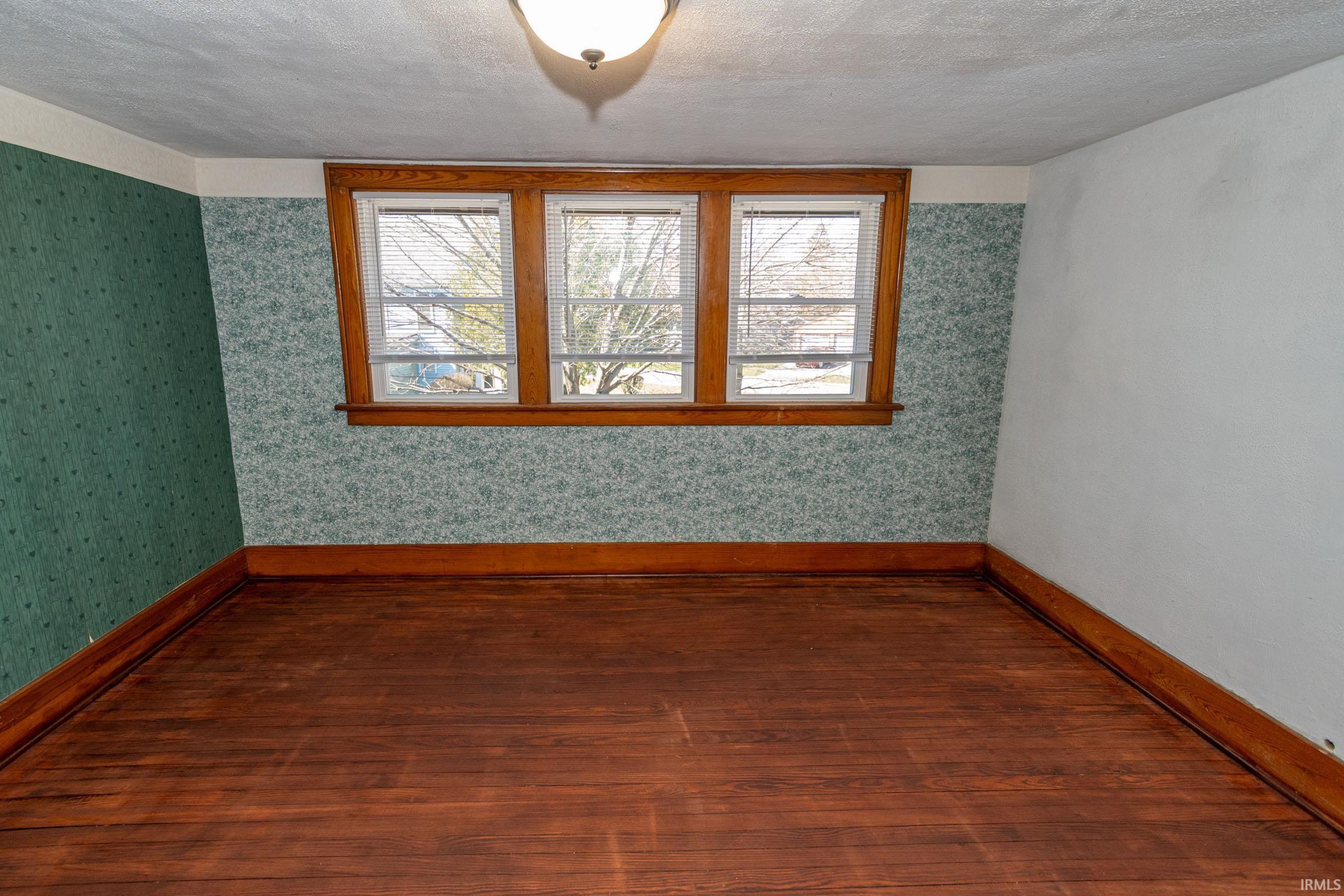 Spare room featuring wood-type flooring, healthy amount of natural light, wallpapered walls, and a textured ceiling