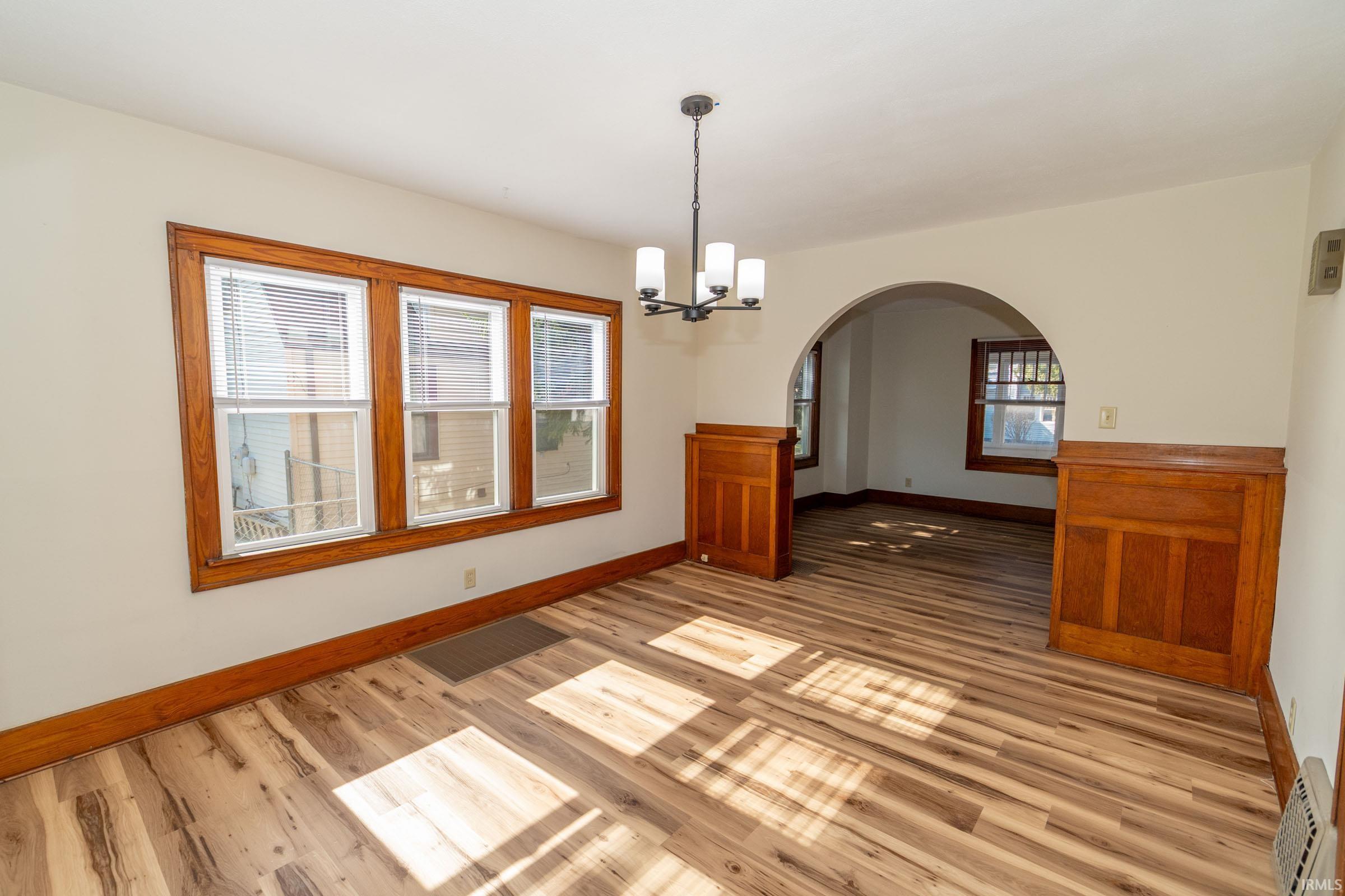 Empty room with a chandelier, arched walkways, and light wood-type flooring