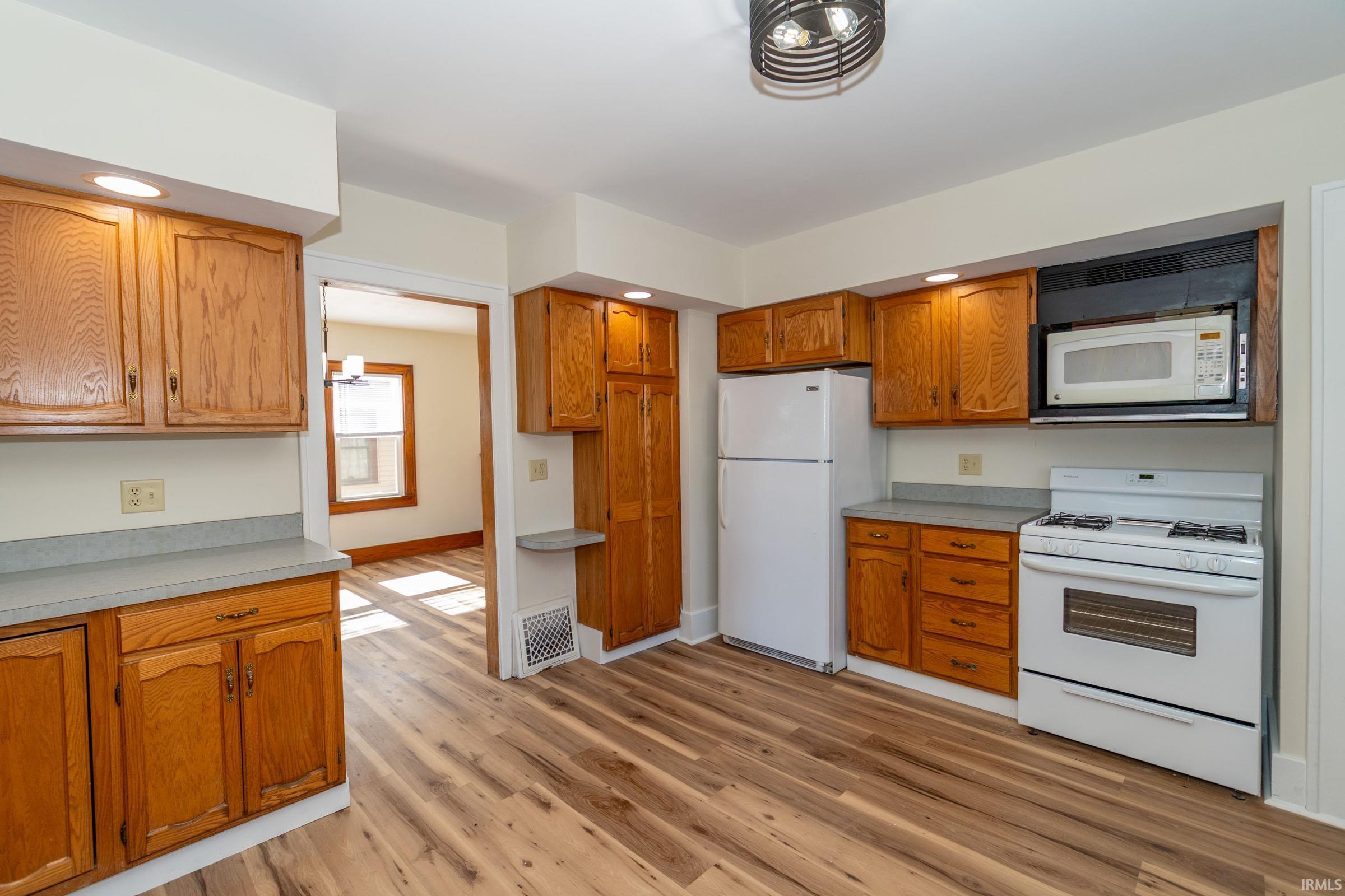 Kitchen featuring white appliances, light countertops, wood finish cabinetry, and light wood-type flooring