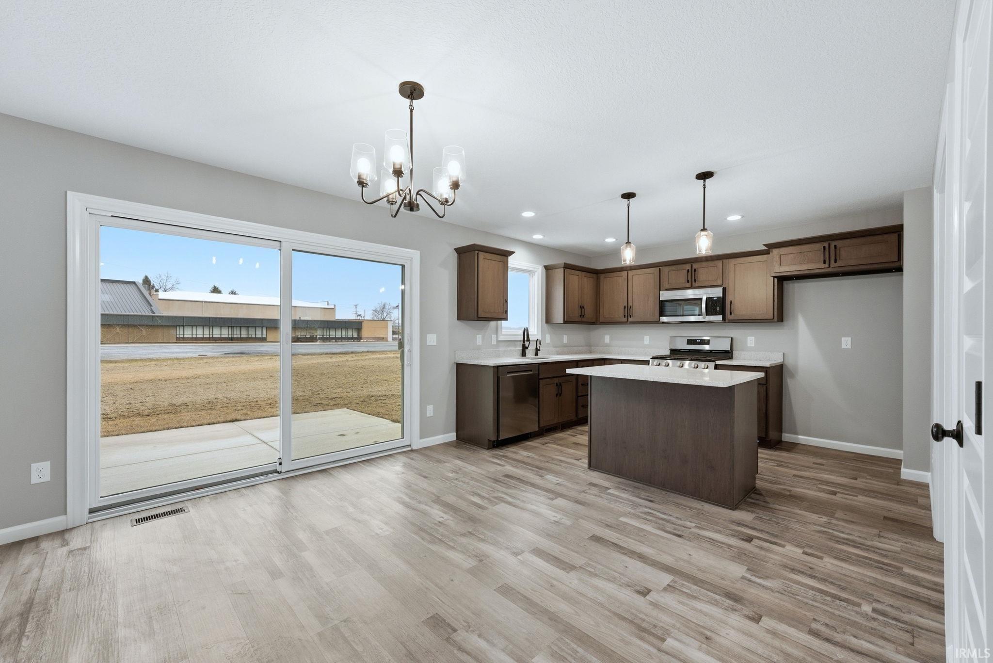 Kitchen with a kitchen island, stainless steel appliances, suspended lighting, and light wood finished floors