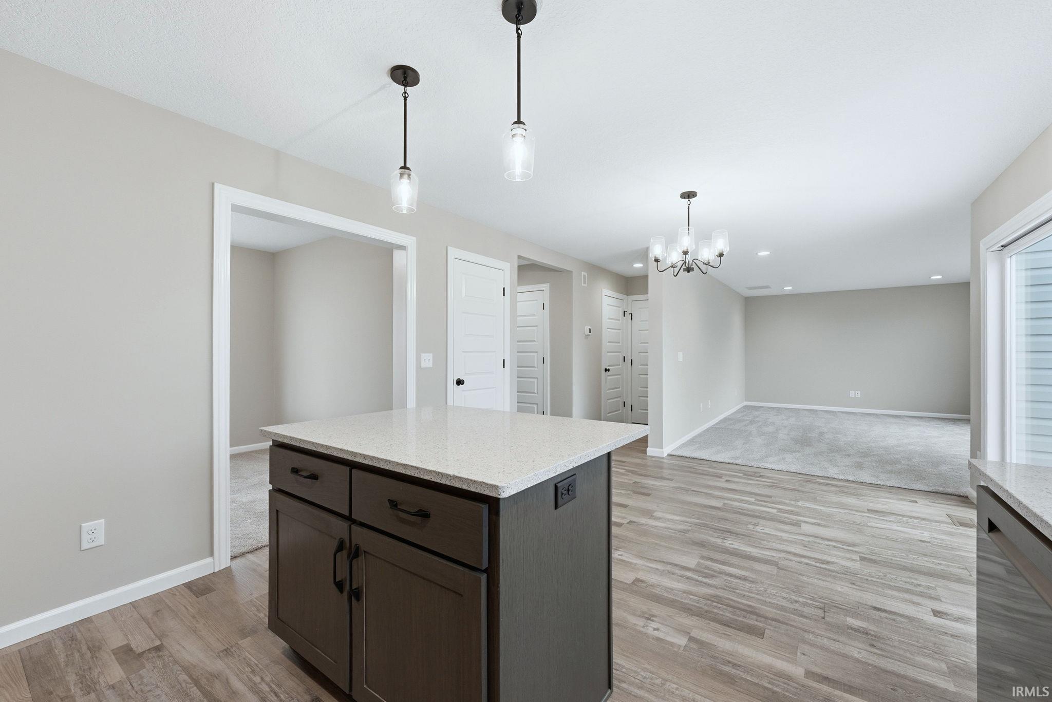 Kitchen featuring a center island, dark wood finish cabinets, light stone counters, dishwasher, and hanging lights