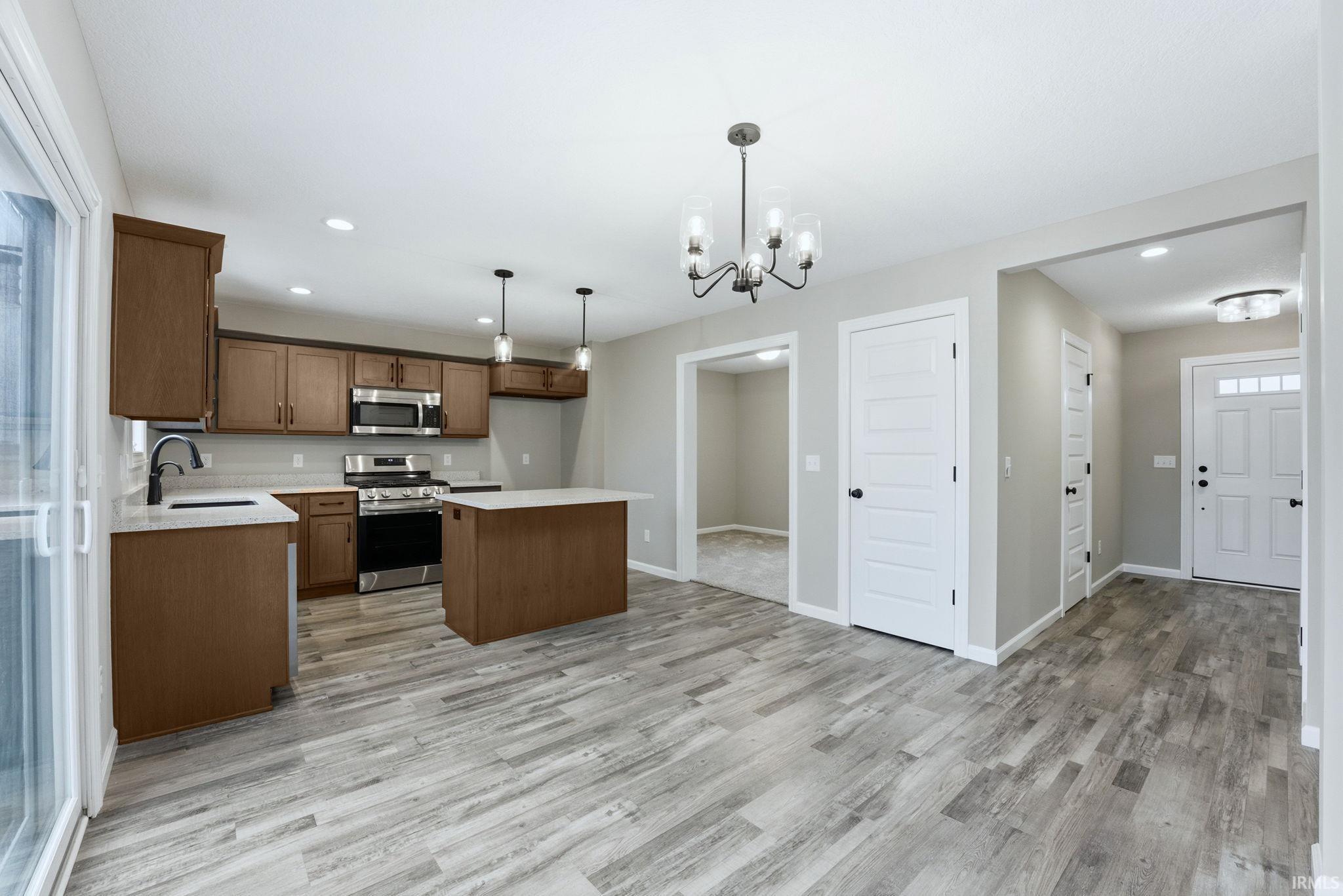 Kitchen featuring stainless steel appliances, a kitchen island, hanging lights, light wood-style floors, and wood finish cabinets