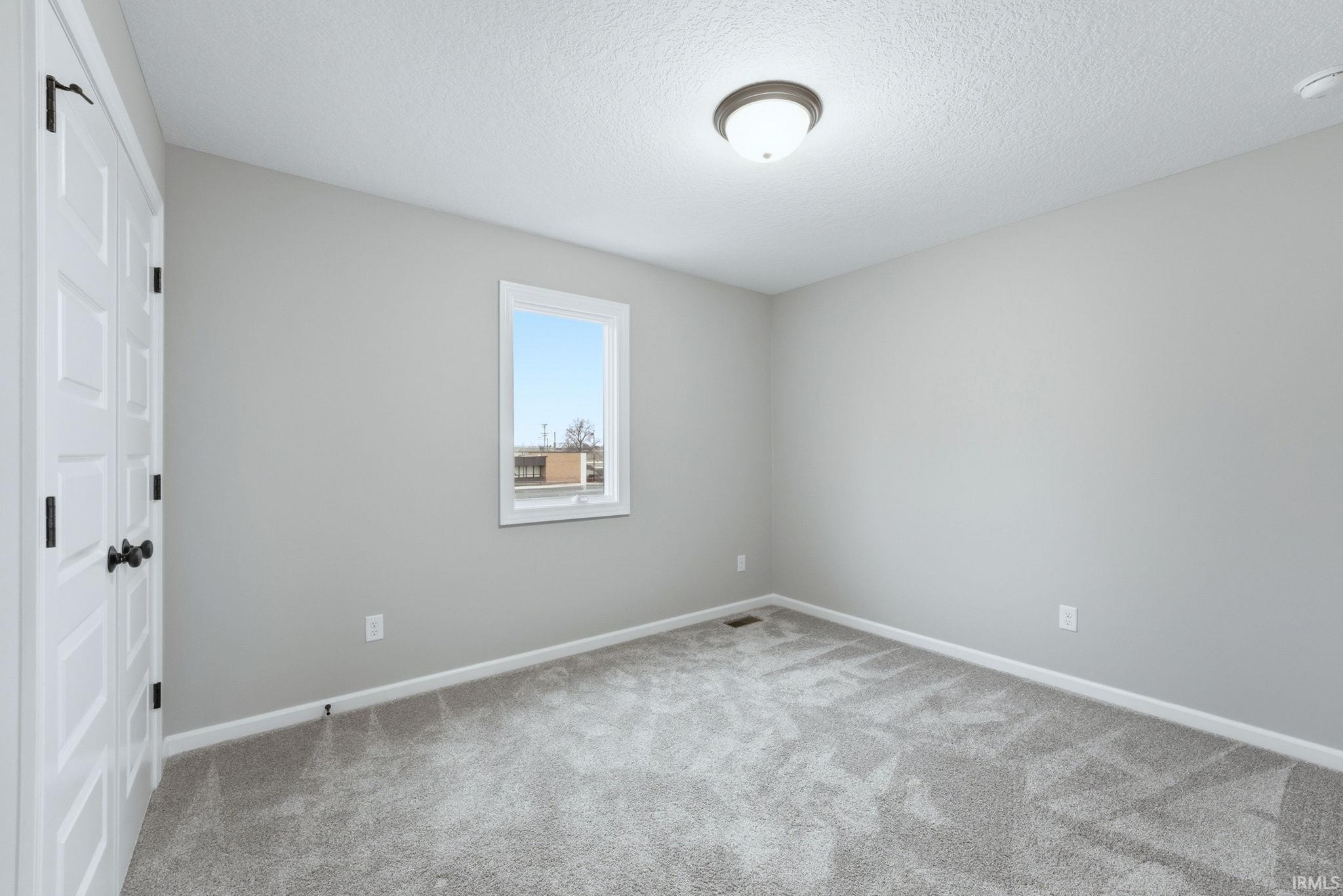 Unfurnished bedroom featuring a closet, a textured ceiling, and light colored carpet