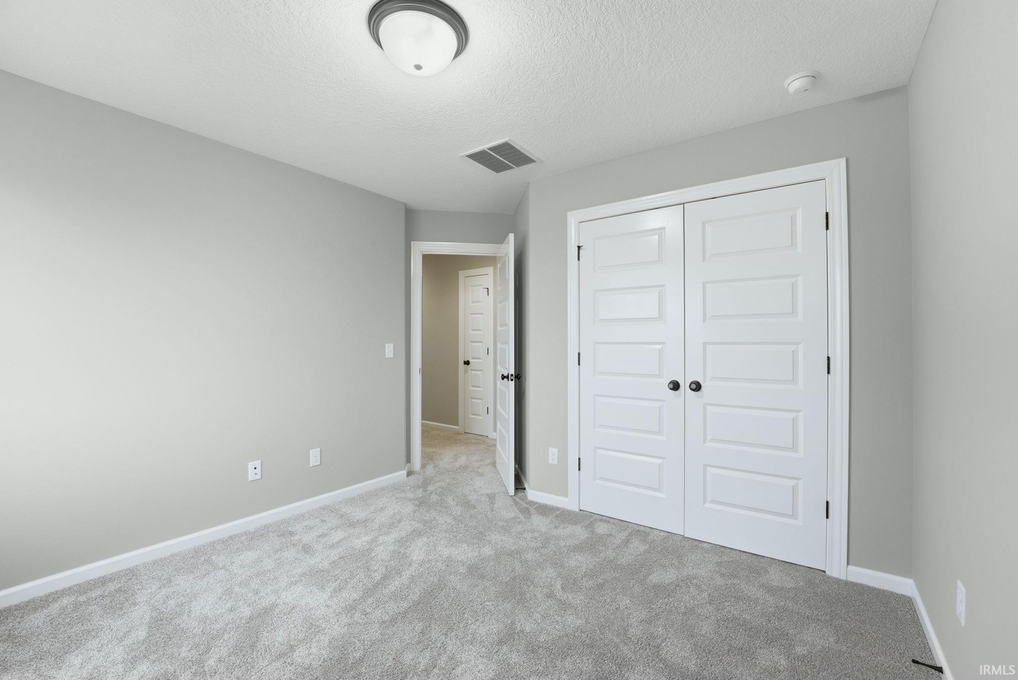 Unfurnished bedroom featuring light carpet, a textured ceiling, and a closet