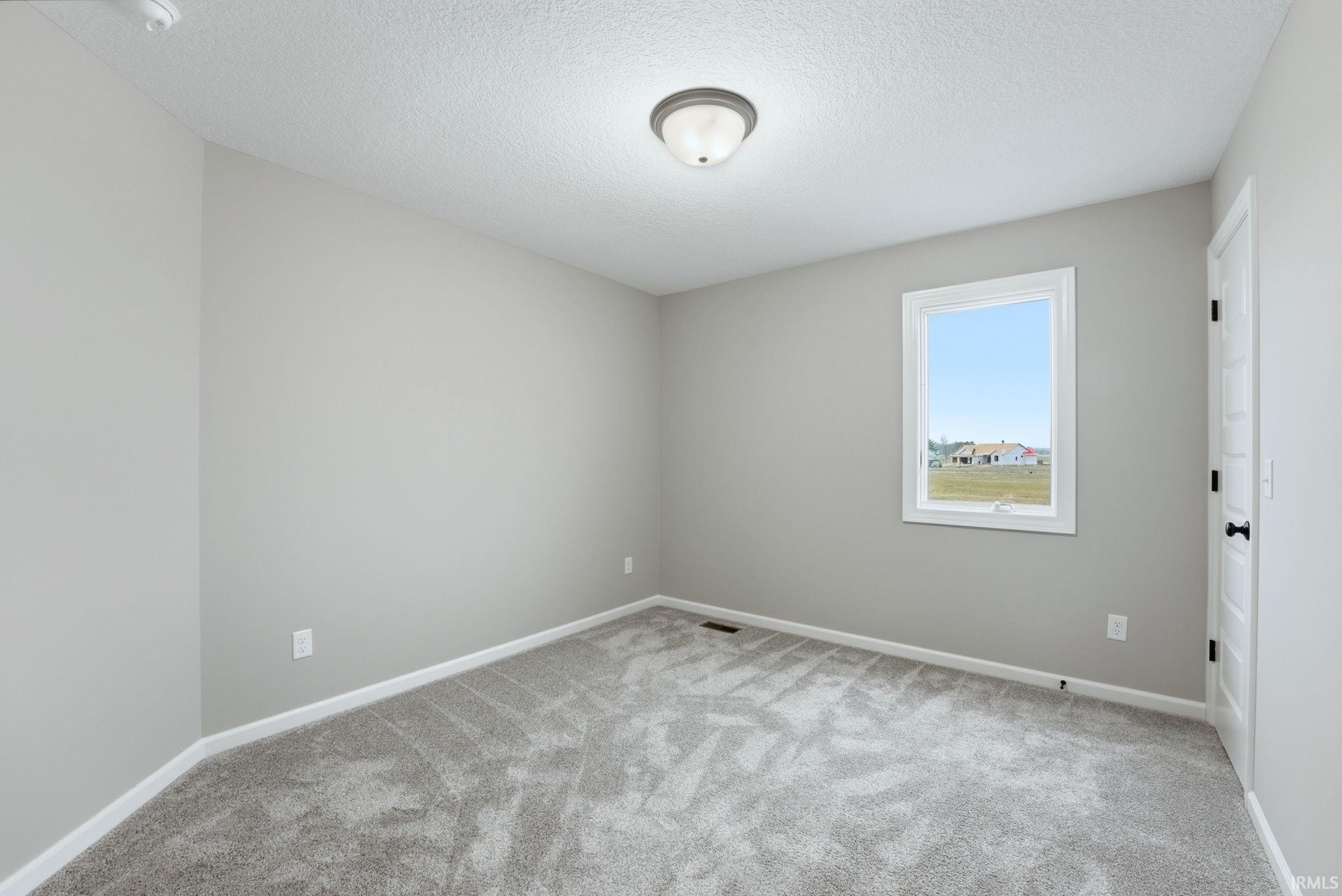 Empty room with light colored carpet and a textured ceiling