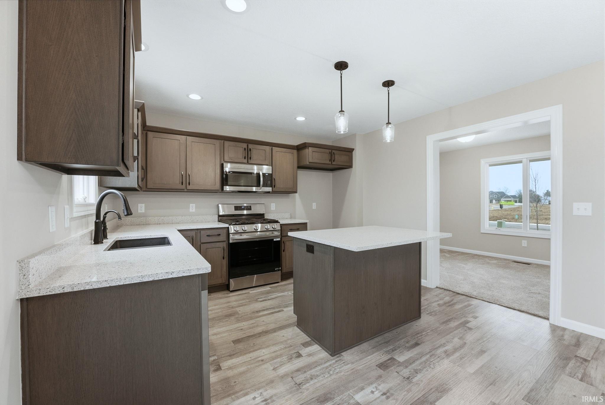 Kitchen featuring stainless steel appliances, a kitchen island, light stone countertops, light wood-type flooring, and dark wood finish cabinets