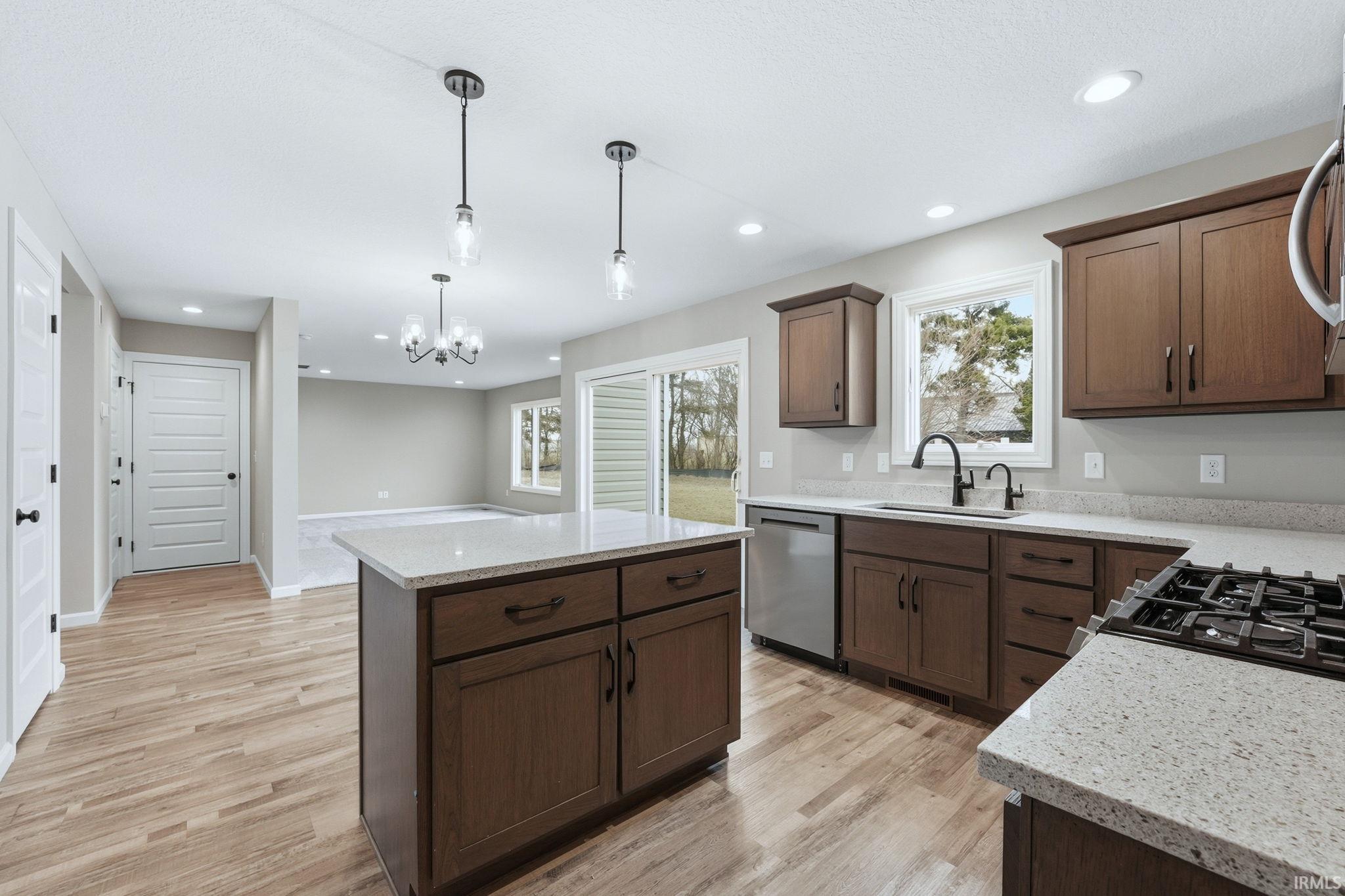 Kitchen with a center island, light stone counters, hanging lights, stainless steel appliances, and light wood-style flooring