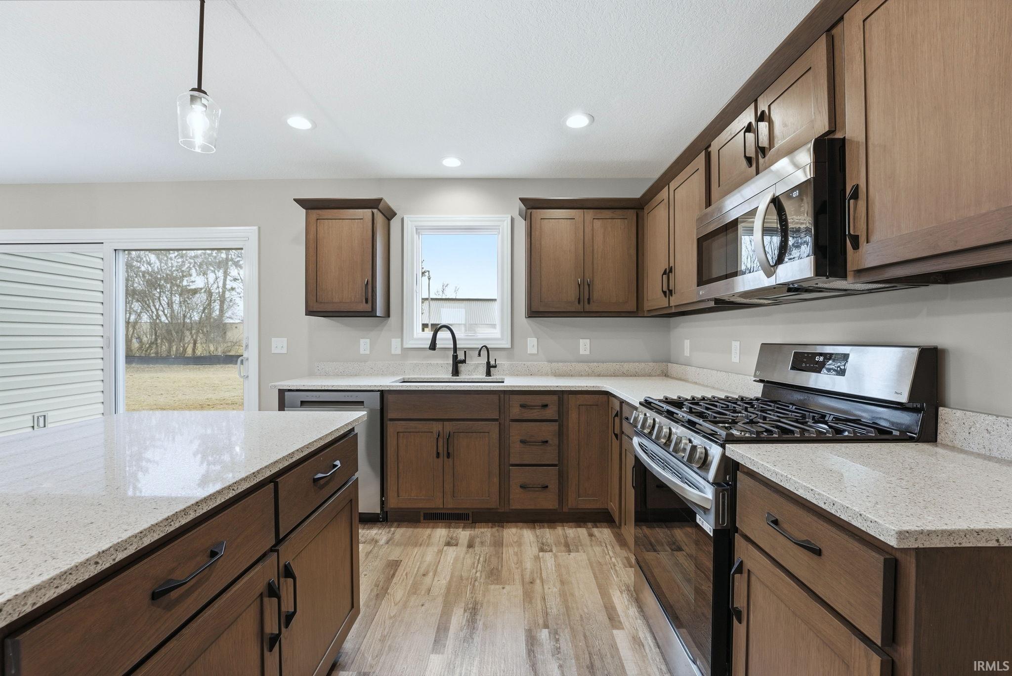 Kitchen featuring stainless steel appliances, hanging light fixtures, light stone counters, and light wood finished floors