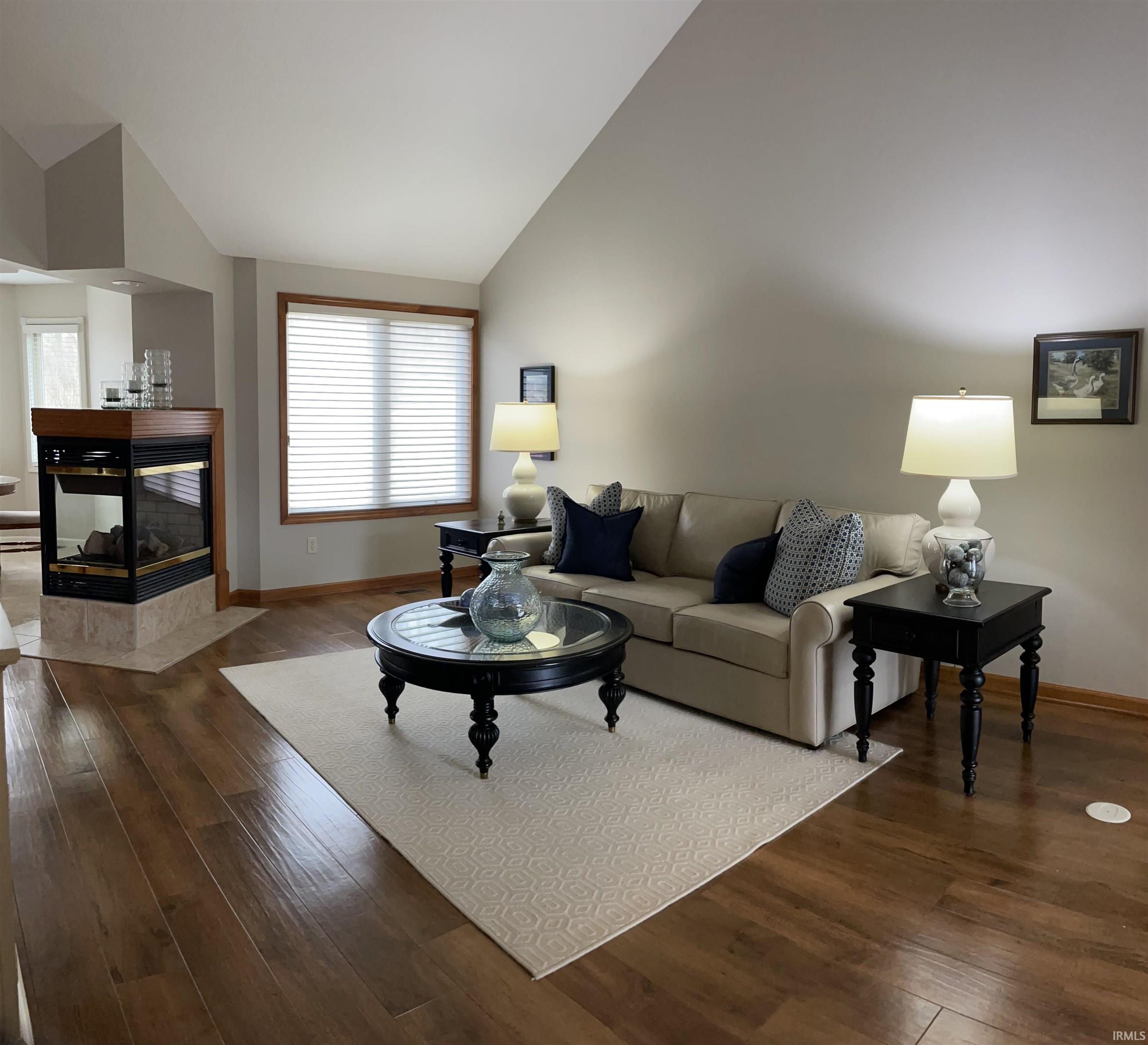 Living area with dark wood-style flooring, vaulted ceiling, and a fireplace