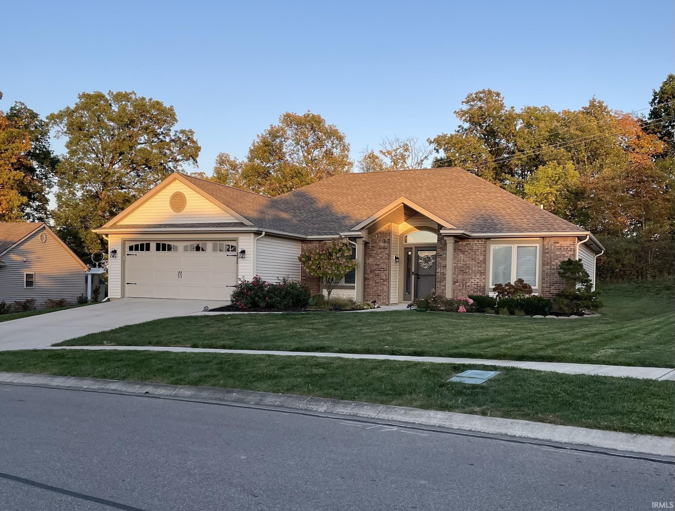 Single story home featuring a front lawn, a garage, driveway, brick siding, and a shingled roof