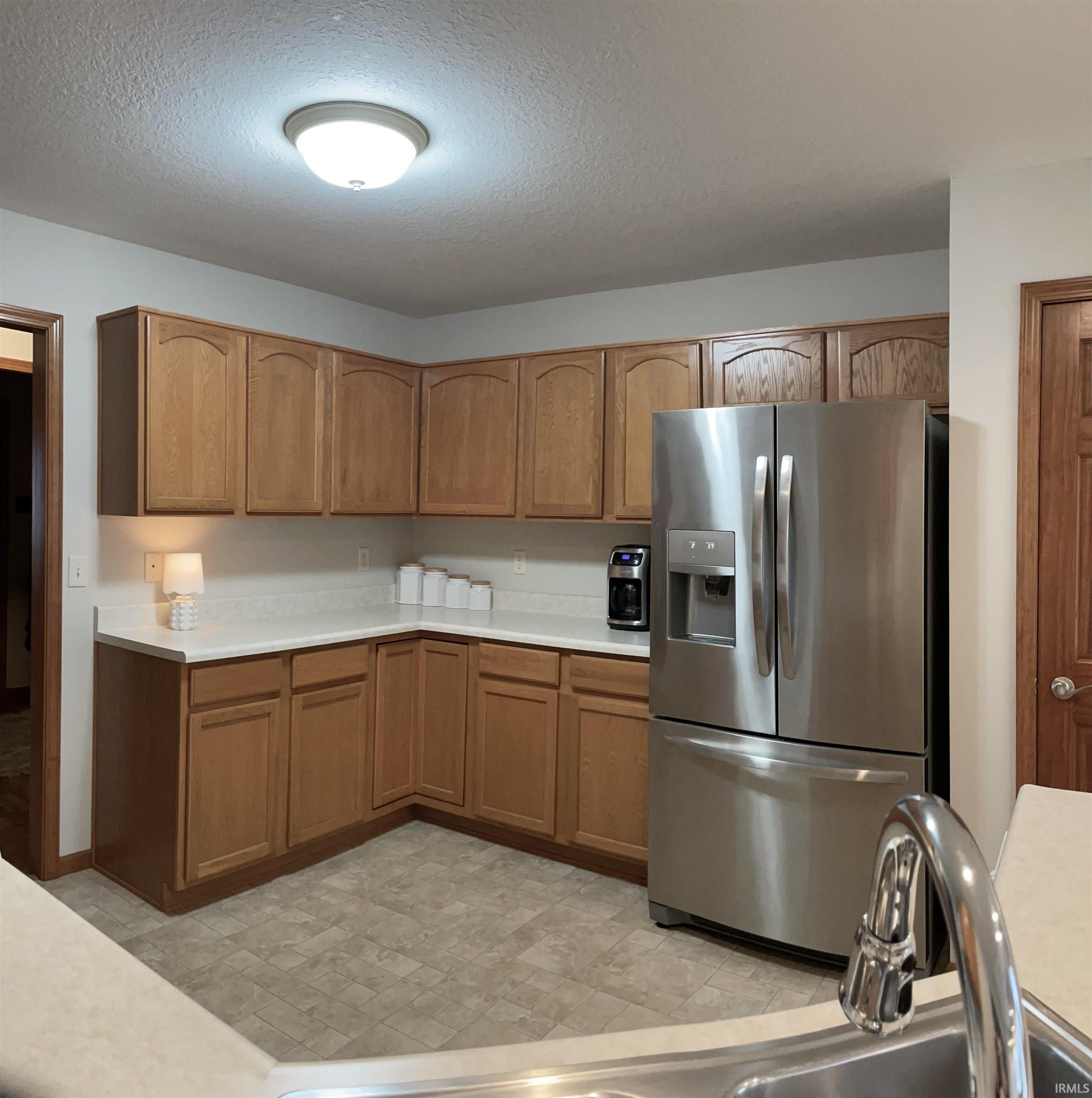Kitchen with stainless steel fridge, light countertops, a textured ceiling, and wood finish cabinetry