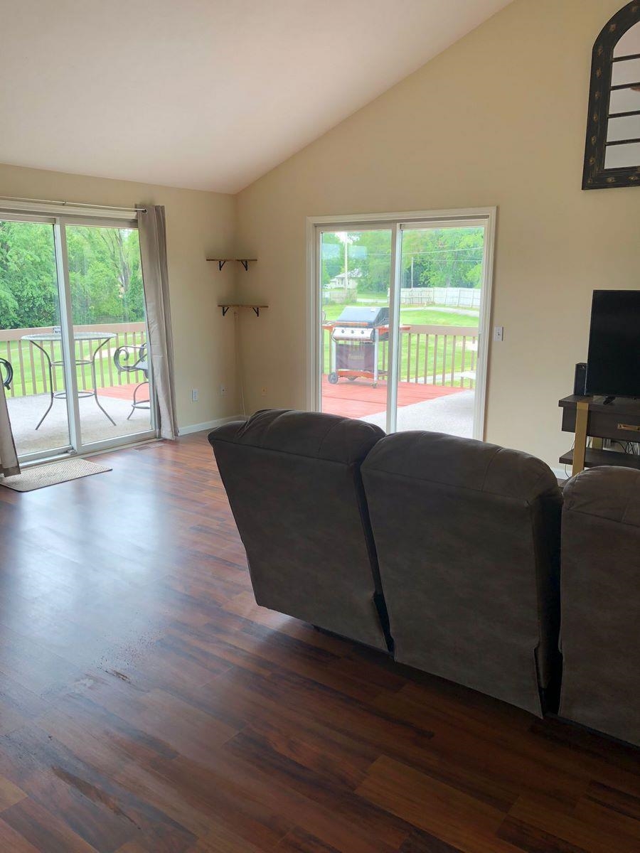 Living room with dark wood-style flooring, vaulted ceiling, and plenty of natural light