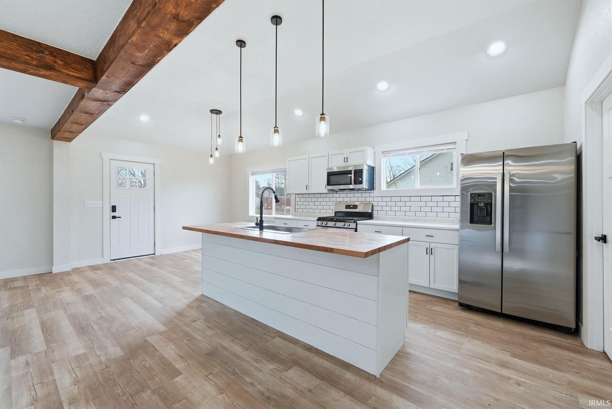 Kitchen with stainless steel appliances, a kitchen island with sink, white cabinetry, backsplash, and wood counters