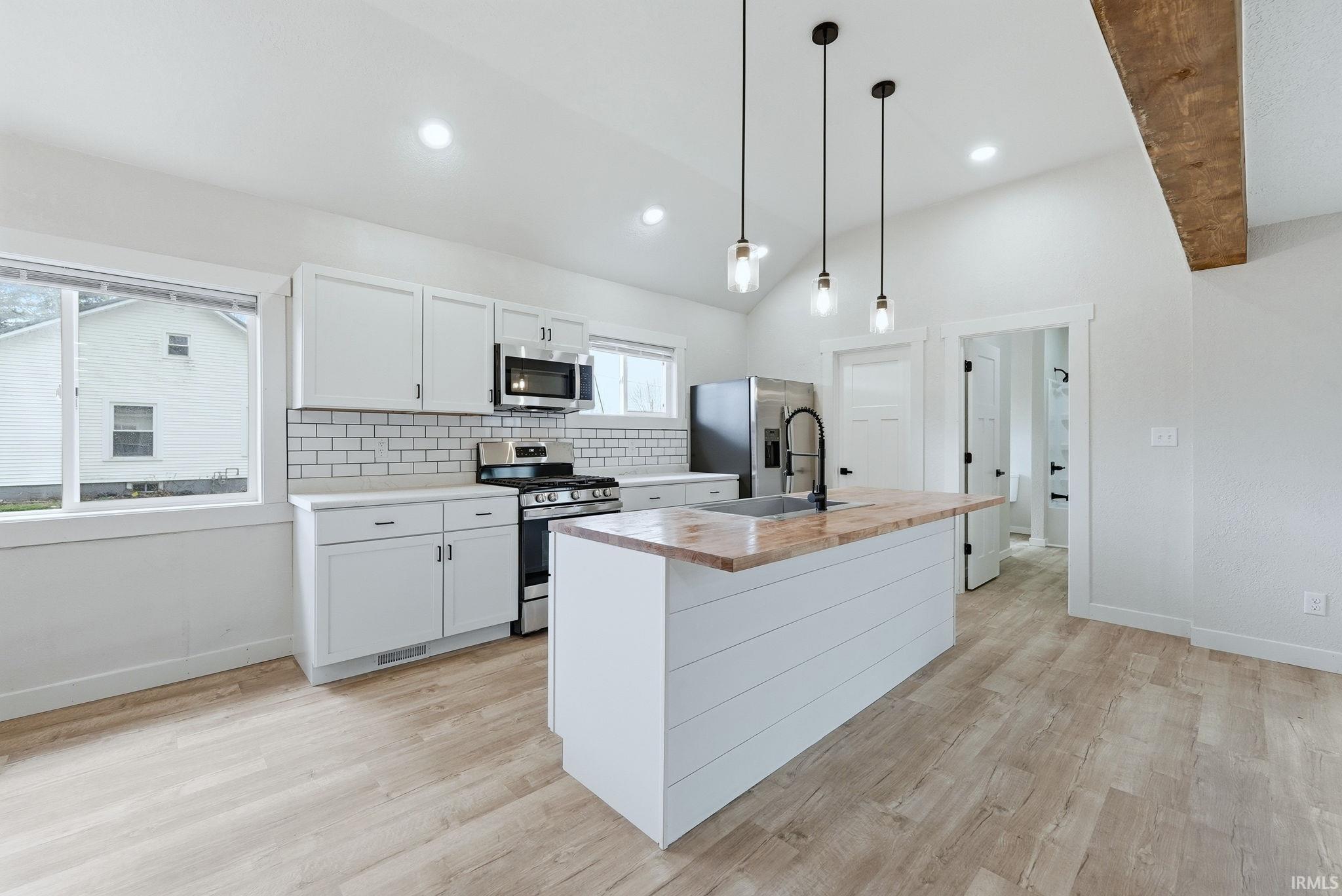 Kitchen featuring decorative backsplash, a center island with sink, stainless steel appliances, white cabinets, and light wood-style floors