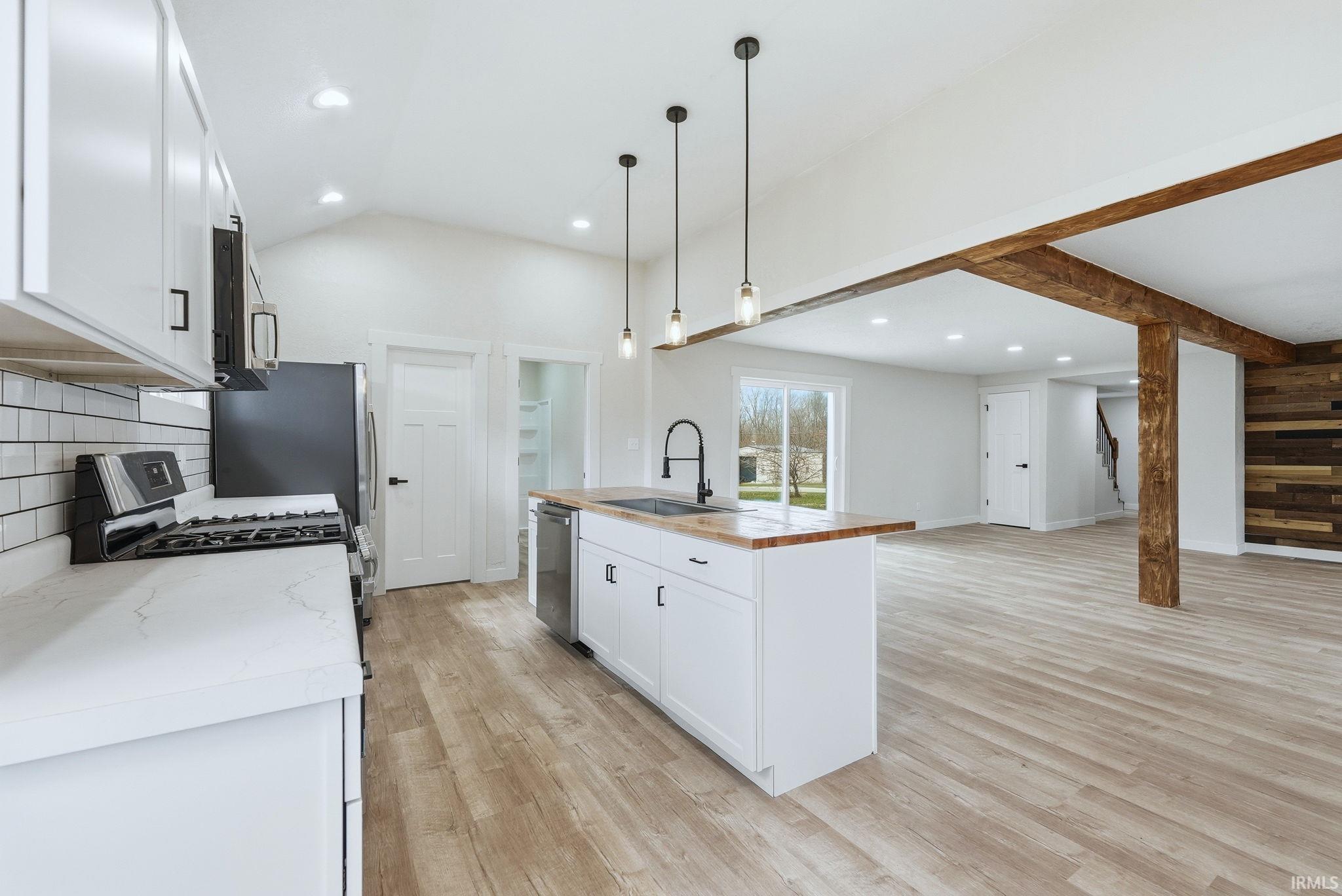 Kitchen with white cabinets, open floor plan, light wood-style flooring, an island with sink, and stainless steel appliances