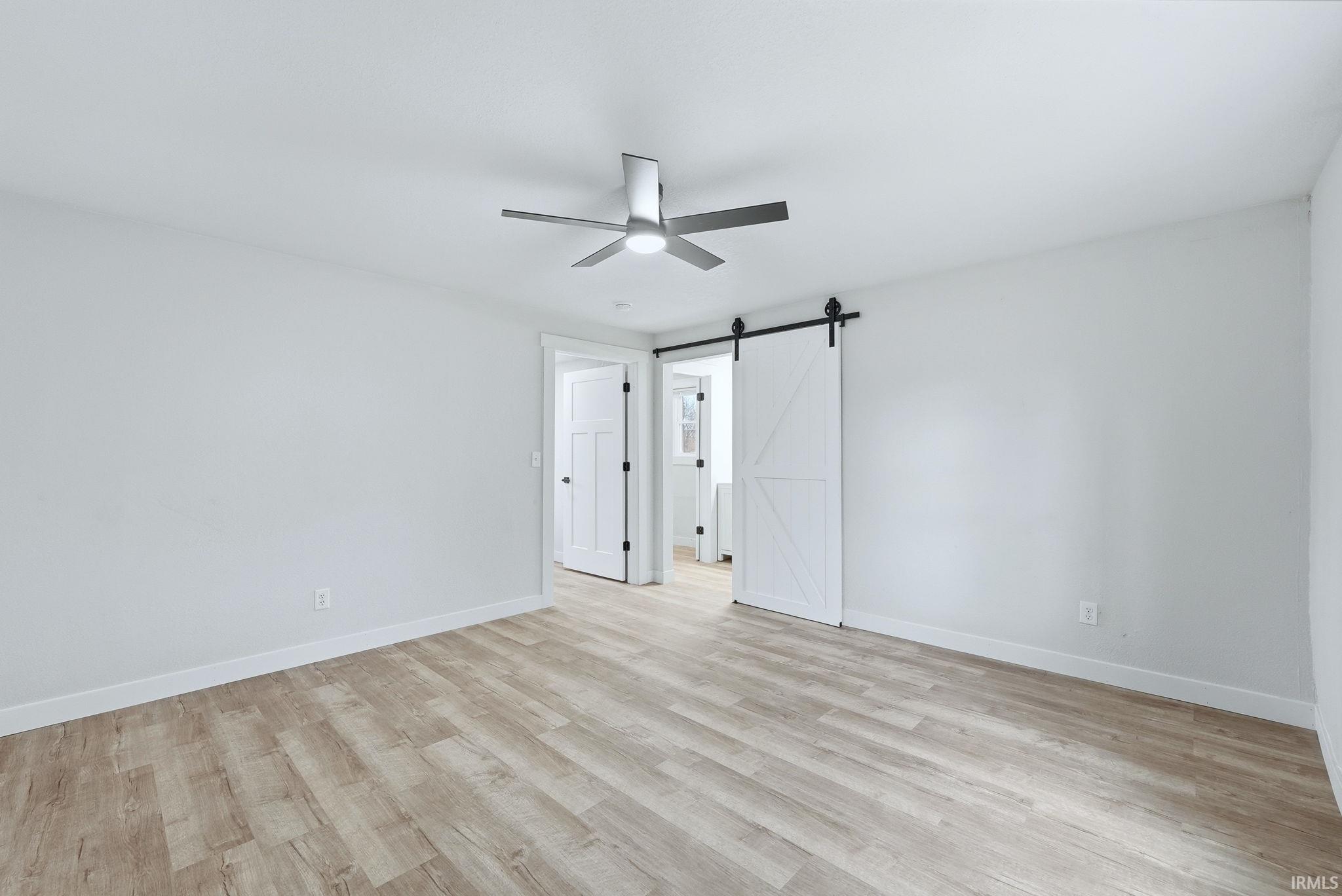 Unfurnished bedroom with a barn door, light wood-style flooring, and a ceiling fan