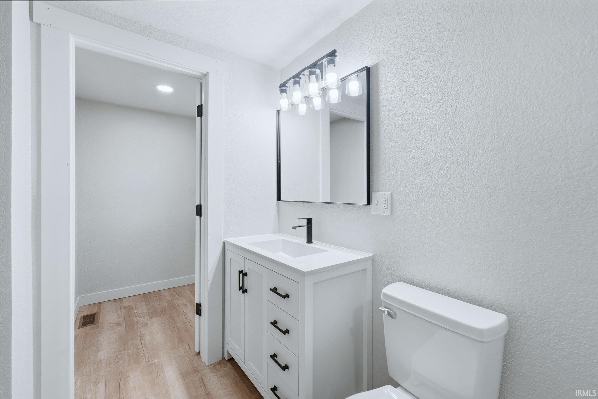 Half bathroom featuring vanity, light wood-style flooring, and a textured wall