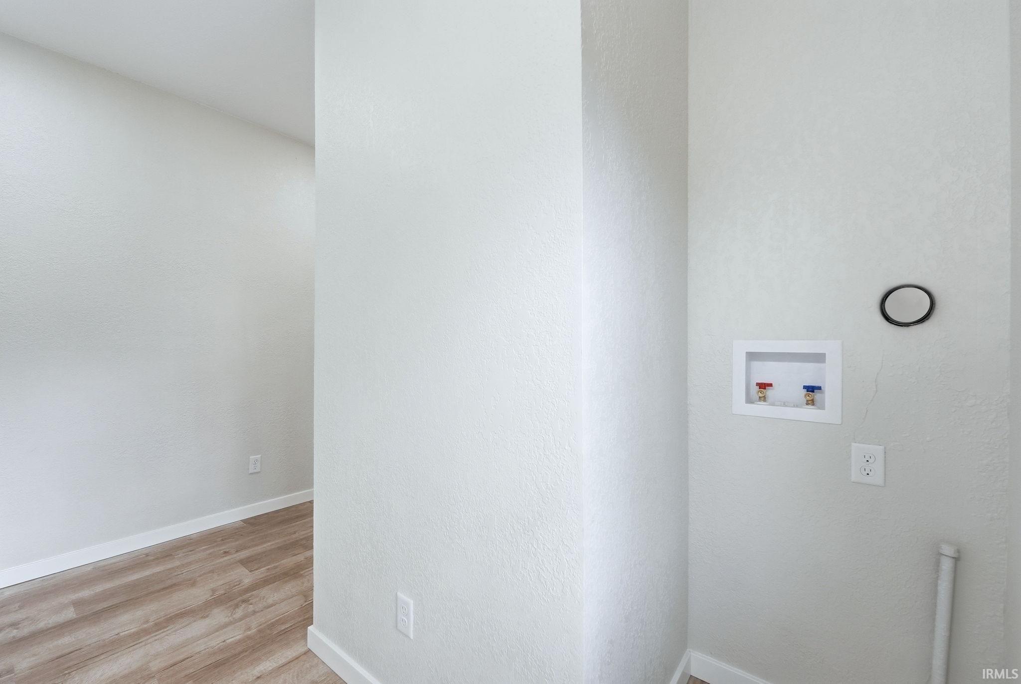 Laundry area featuring washer hookup, light wood finished floors, and a textured wall