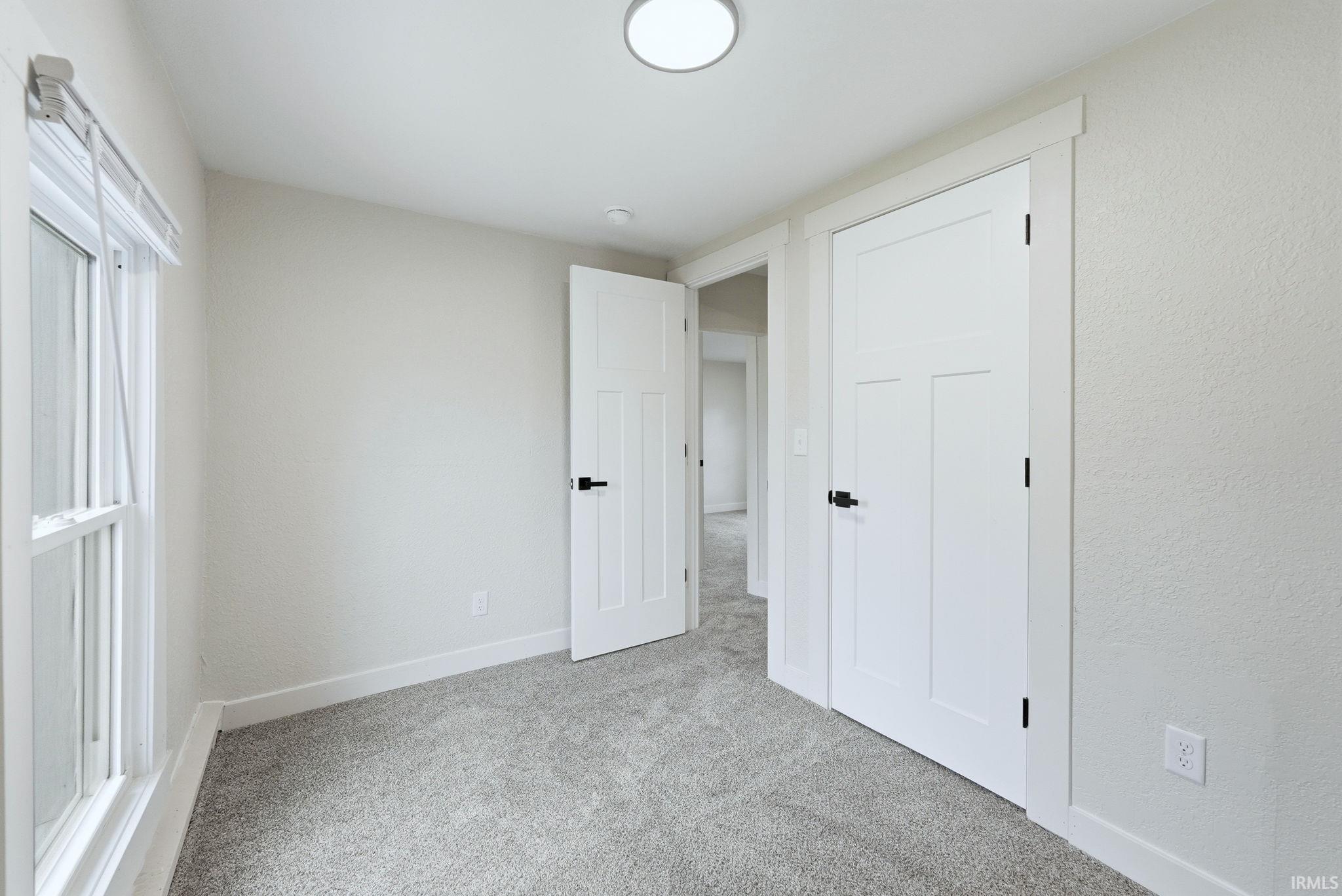 Unfurnished bedroom with light colored carpet and a textured wall