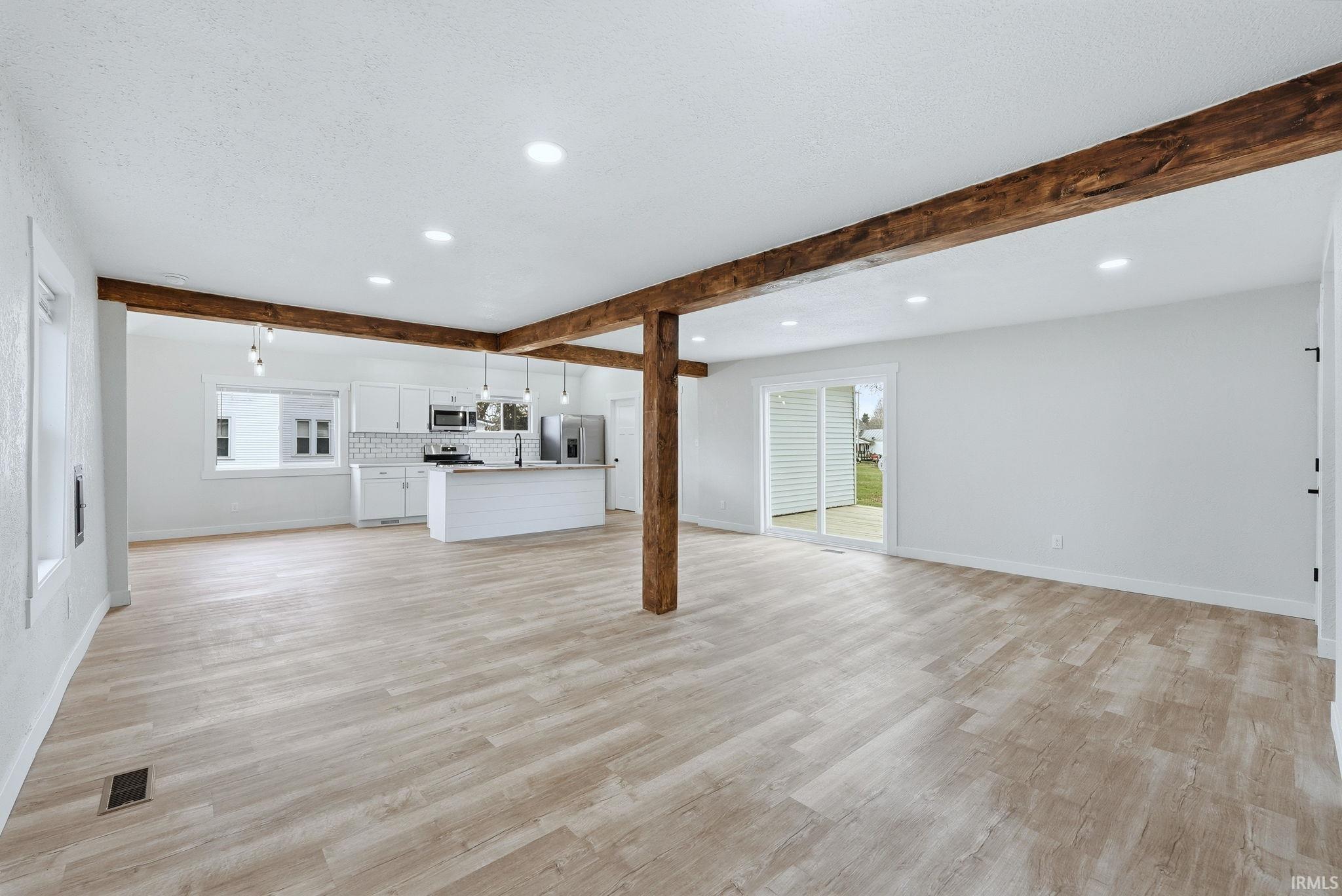 Unfurnished living room featuring recessed lighting, beamed ceiling, light wood-style flooring, and a textured ceiling