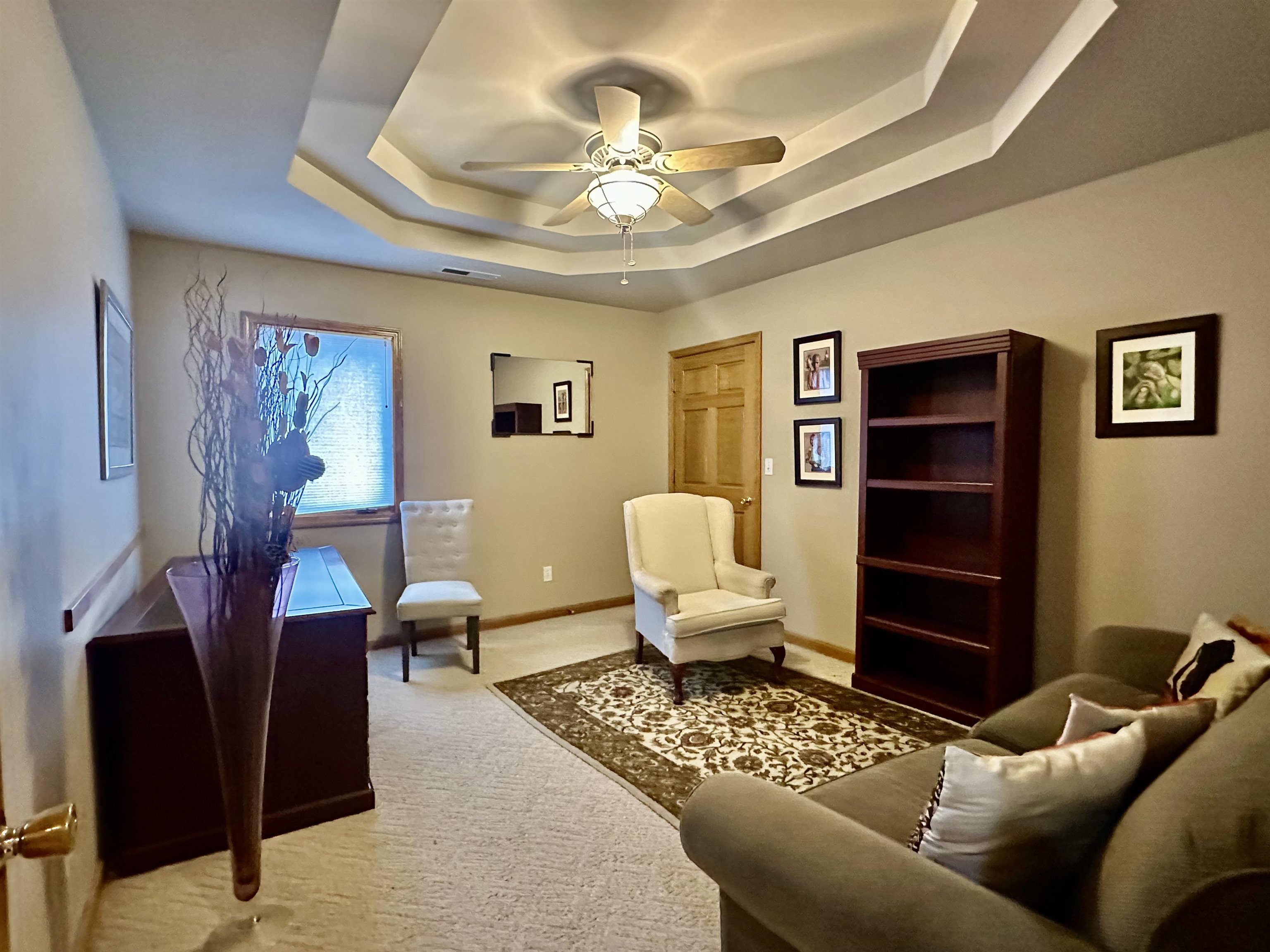 Office with a ceiling fan, carpet, and a tray ceiling