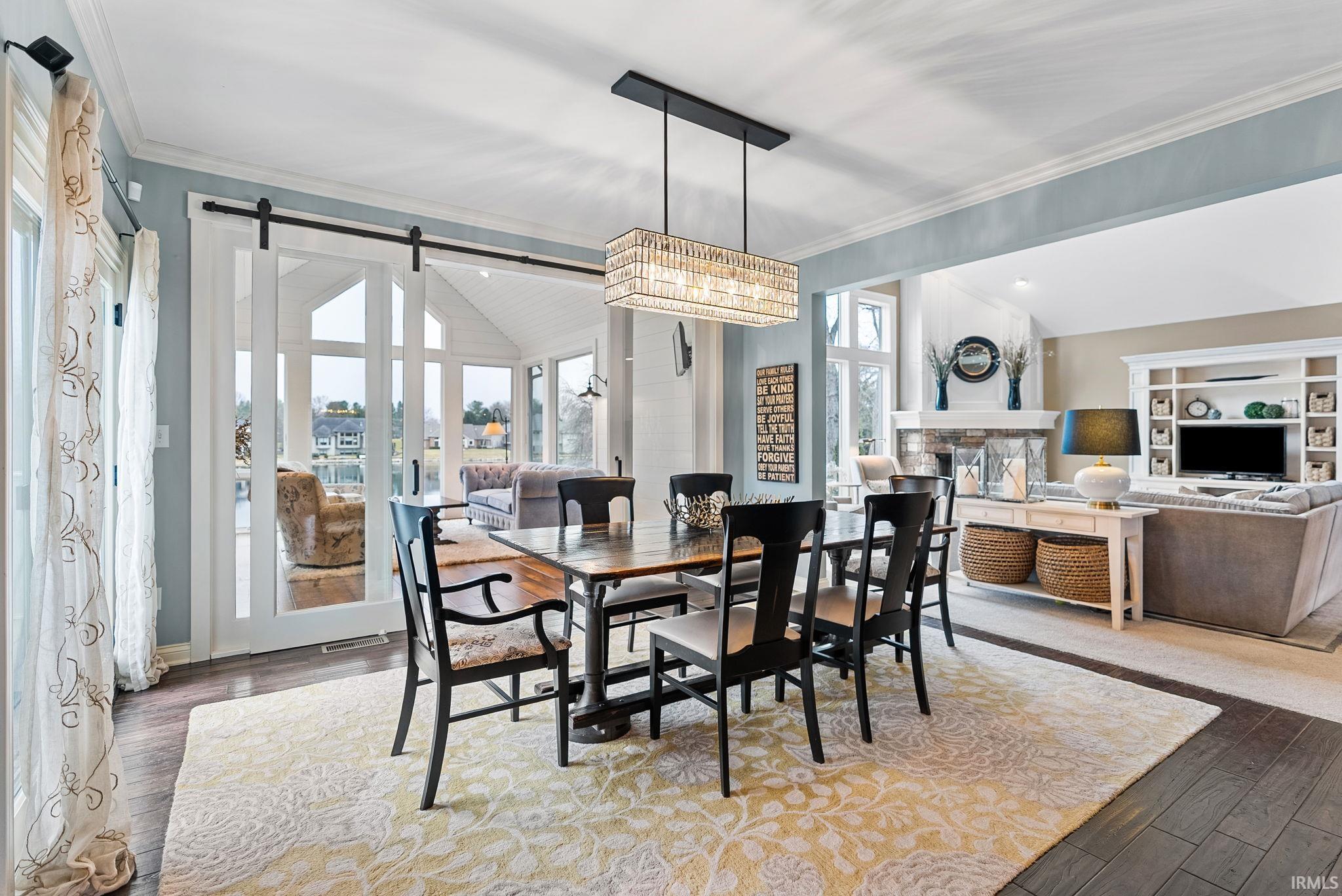 Dining space with ornamental molding, a stone fireplace, wood finished floors, and a barn door