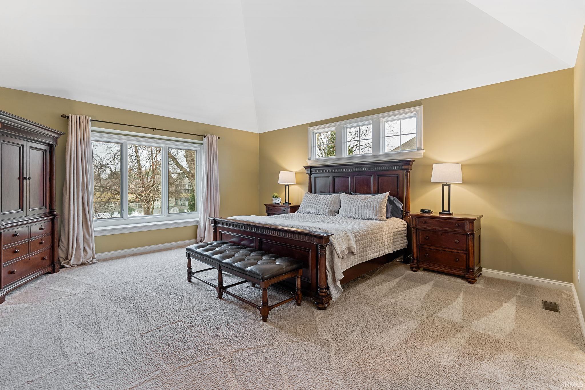 Bedroom with light carpet, multiple windows, and lofted ceiling