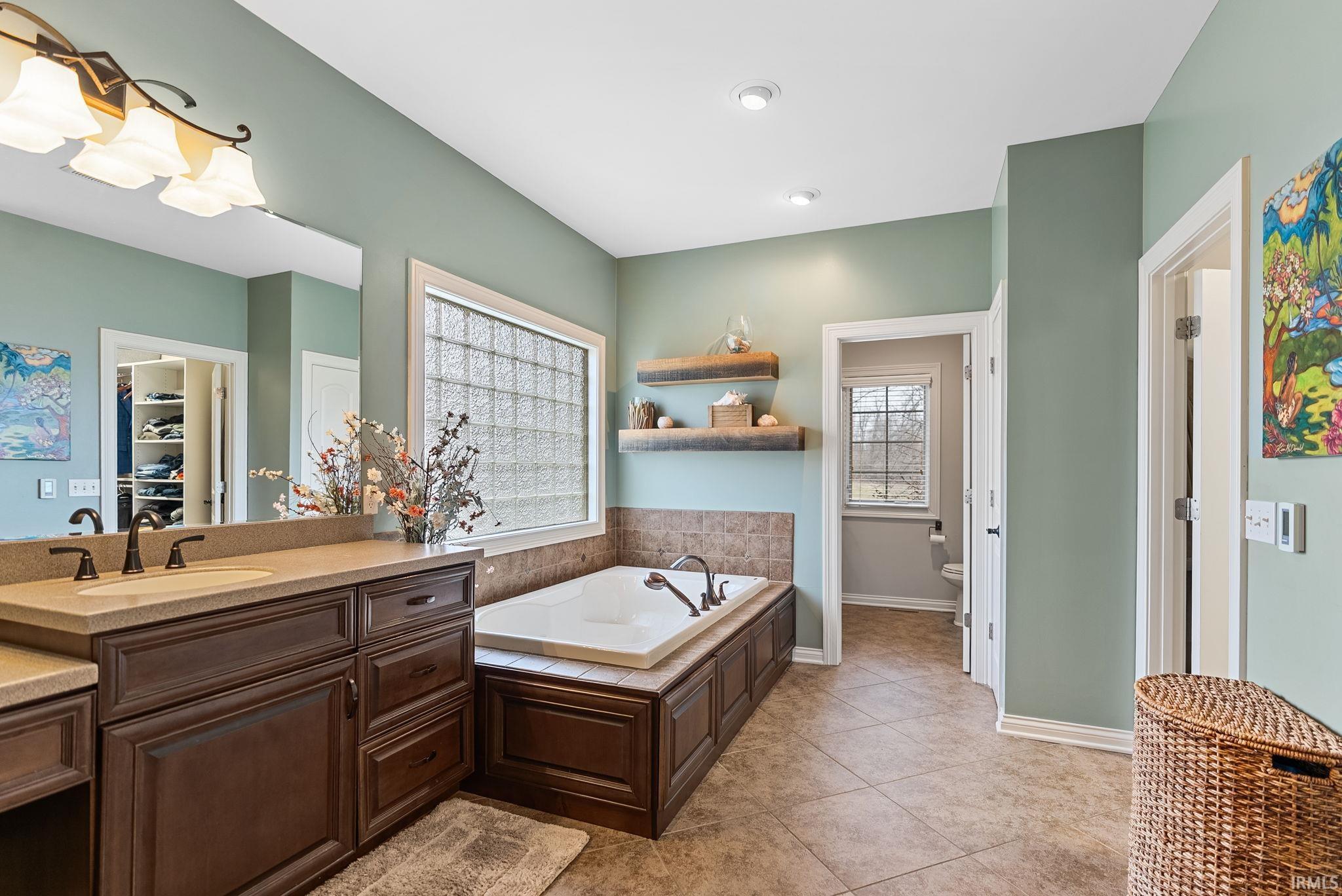 Full bath featuring vanity, light tile patterned flooring, a garden tub, and a spacious closet