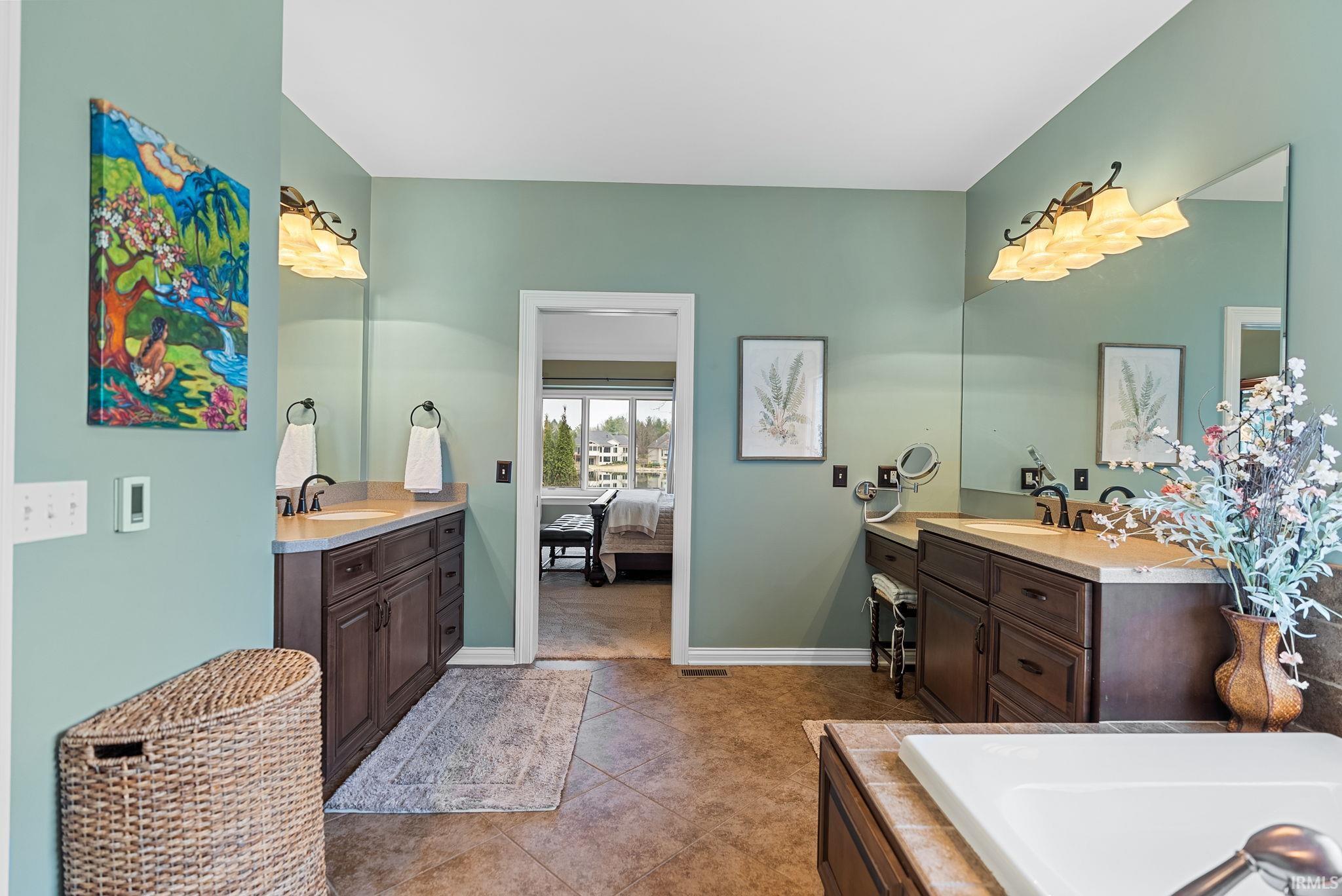 Ensuite bathroom with two vanities, a bath, and dark tile patterned flooring