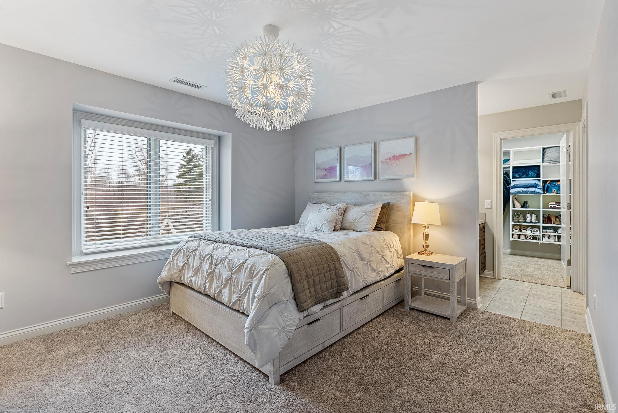 Bedroom featuring light carpet, a spacious closet, and hanging lights